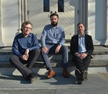 Three people sitting on steps outside a building in daylight