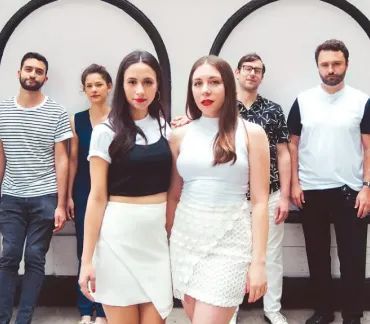Five people posing outdoors in front of a wall, with two women centered in white and black outfits.