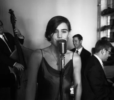 Singer at a vintage microphone performing in front of a jazz band in a black-and-white scene