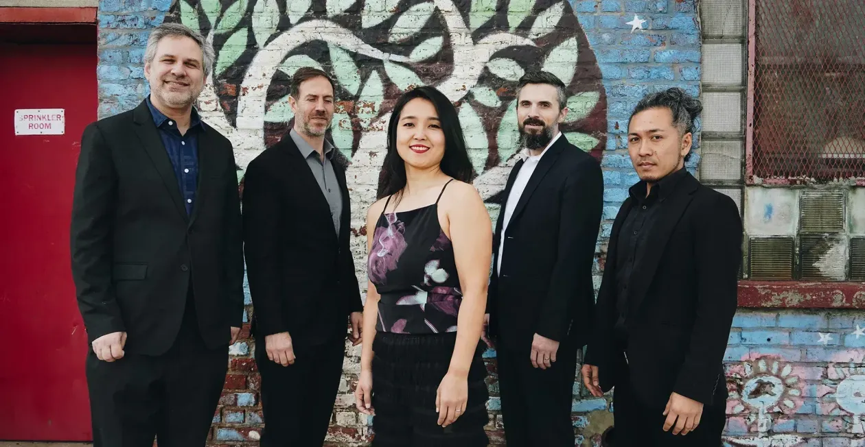 Five people standing in front of a colorful mosaic wall, dressed in formal evening wear.