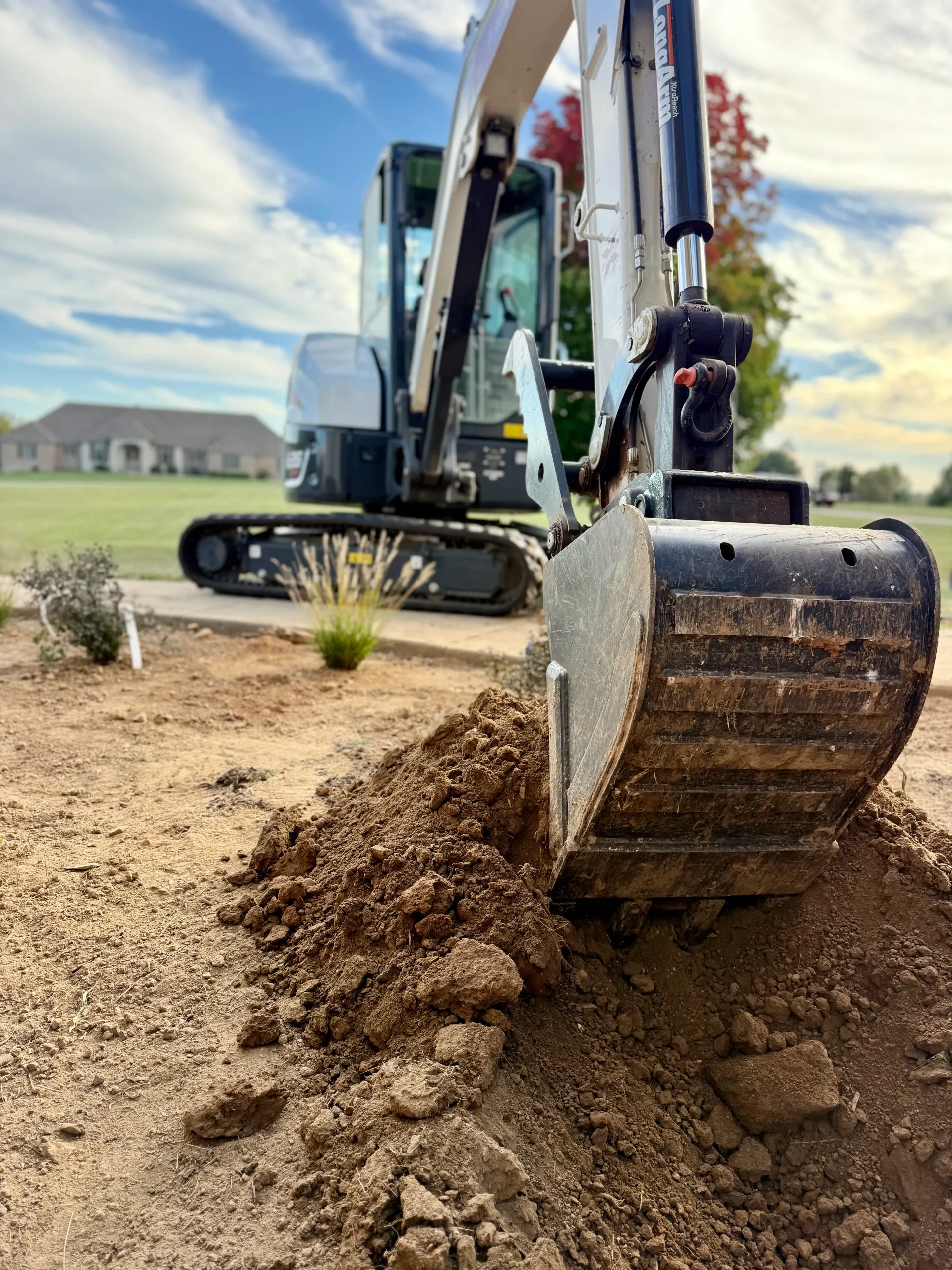 A close-up of an excavator bucket digging into dirt with the rest of the machinery visible in the background.