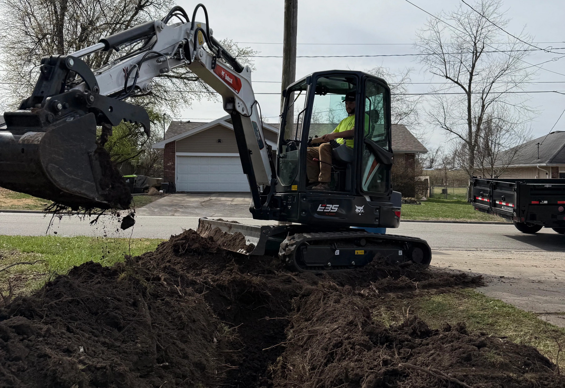A white Bobcat compact excavator digging a trench in a residential yard. Springfield MO