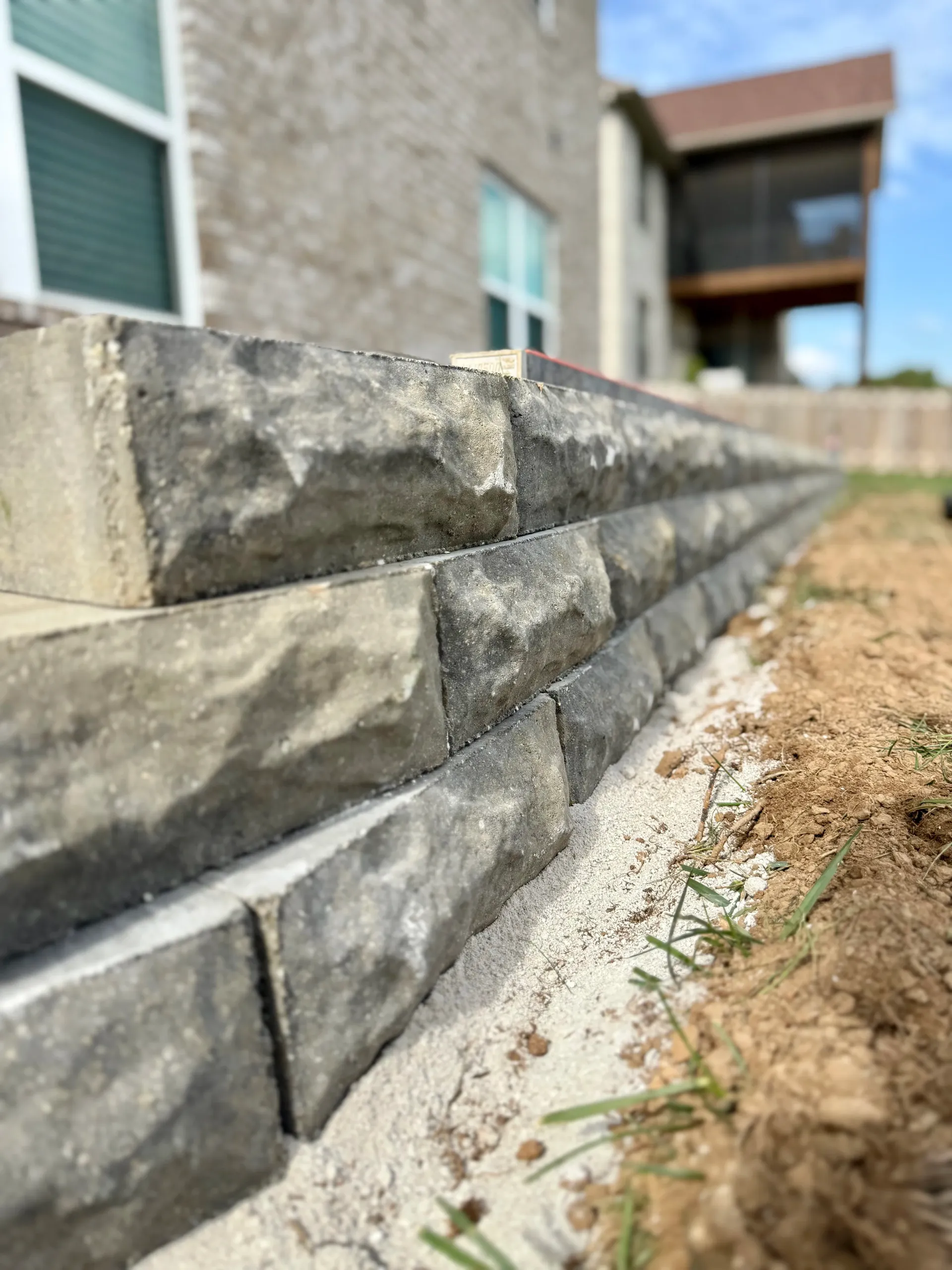 A low, stacked-stone retaining wall sits on a gravel base next to a house with a blurred background. Springfield