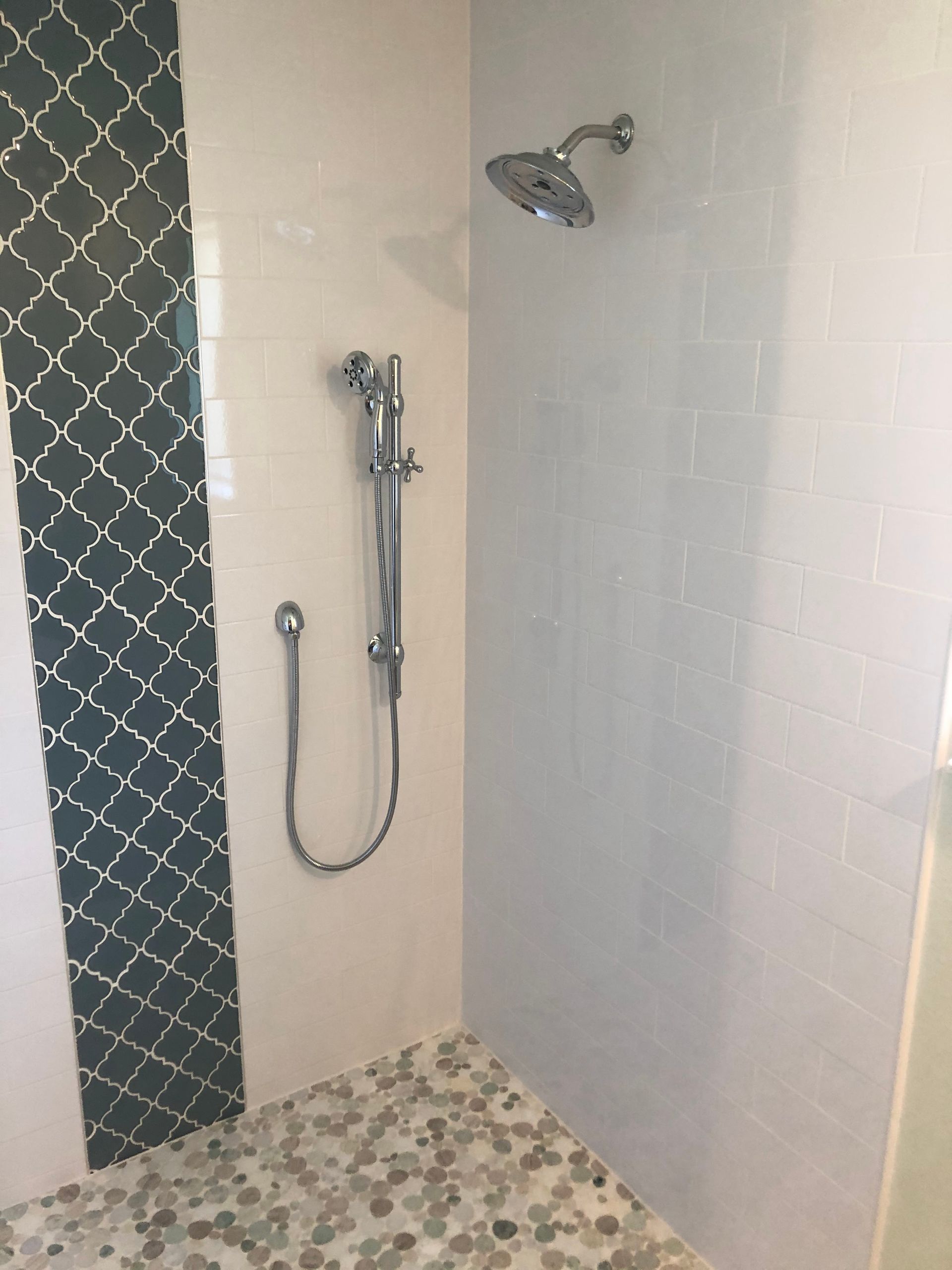 Shower stall with teal accent tile and pebble floor. Chrome shower fixtures on white tiled walls.