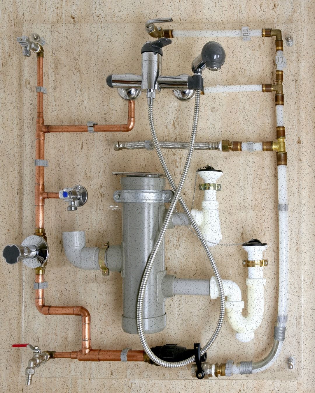 Plumbing pipes and fixtures mounted on a tan surface, including faucets, sink trap, and showerhead.