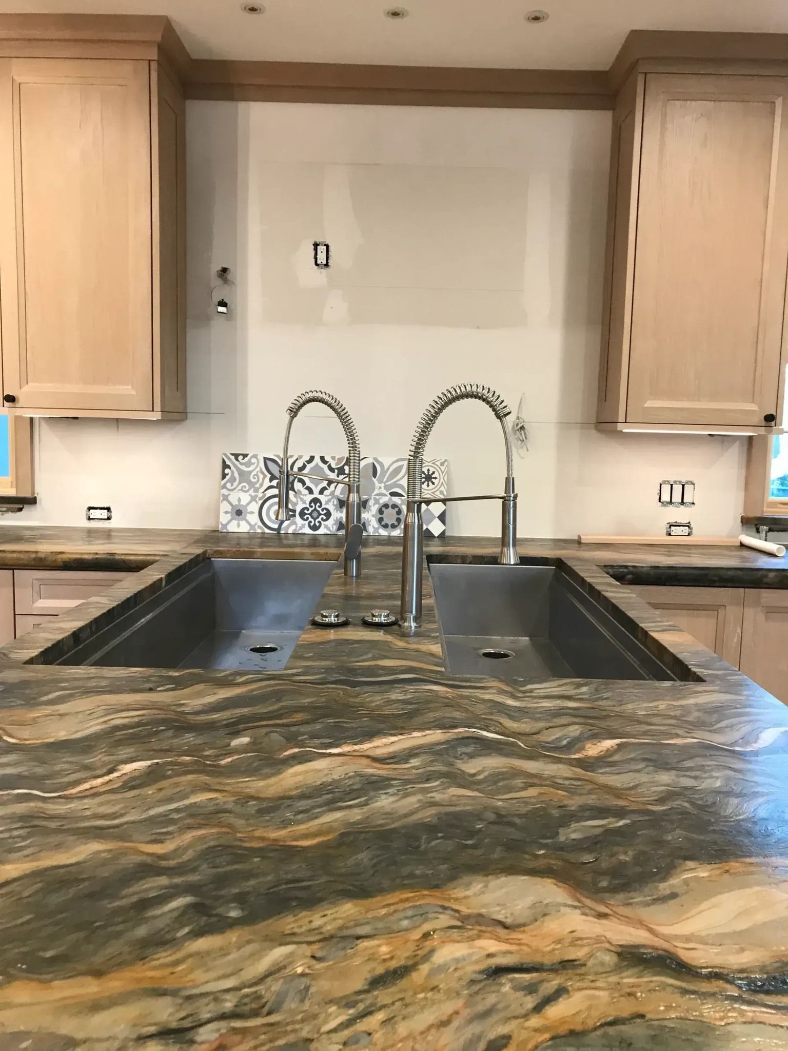 Kitchen with a dual sink, granite countertop, and cabinets. Backsplash is partially tiled.