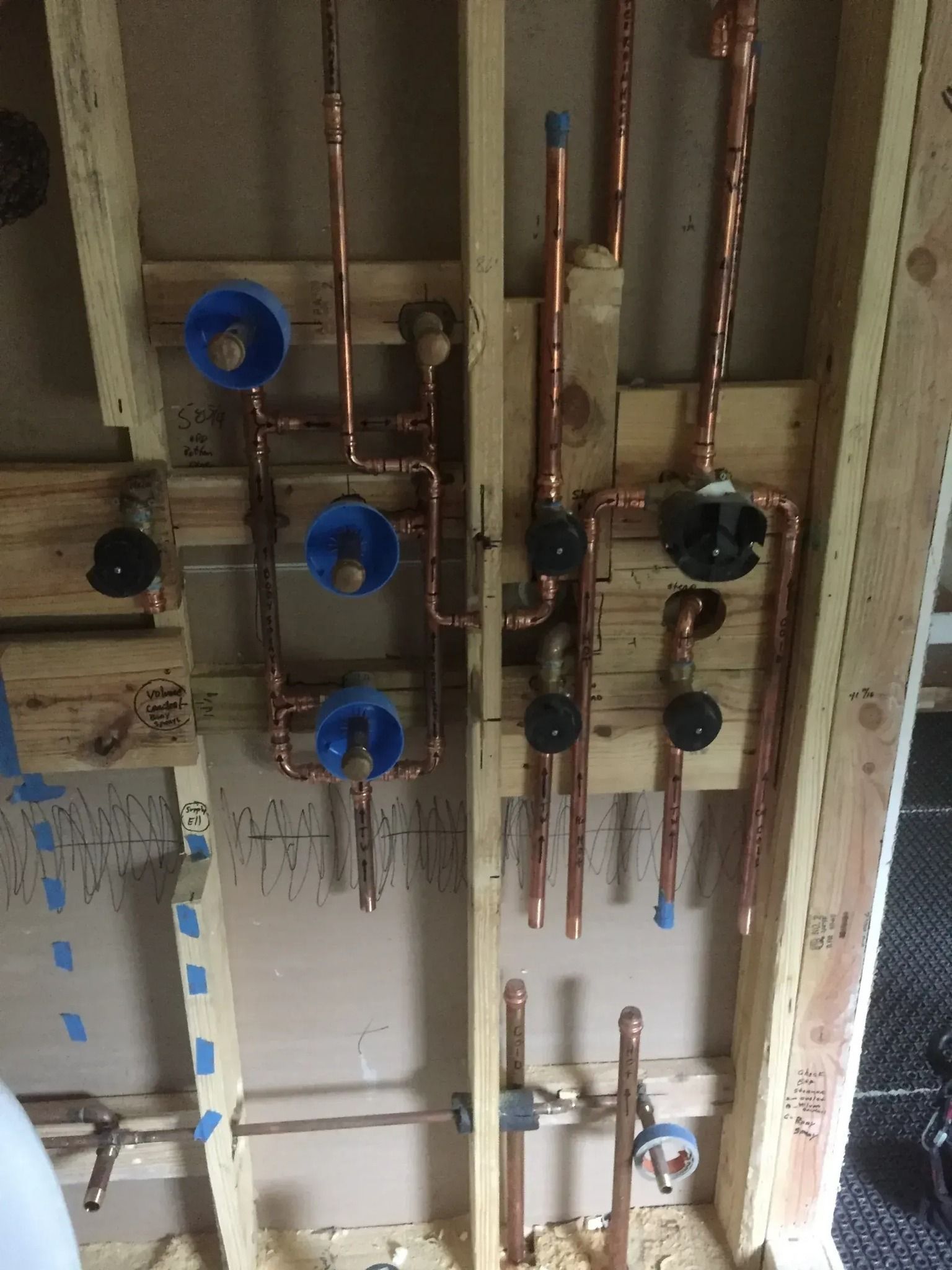 Copper pipes and plumbing fixtures installed in a wooden wall frame. Blue and black components are visible.