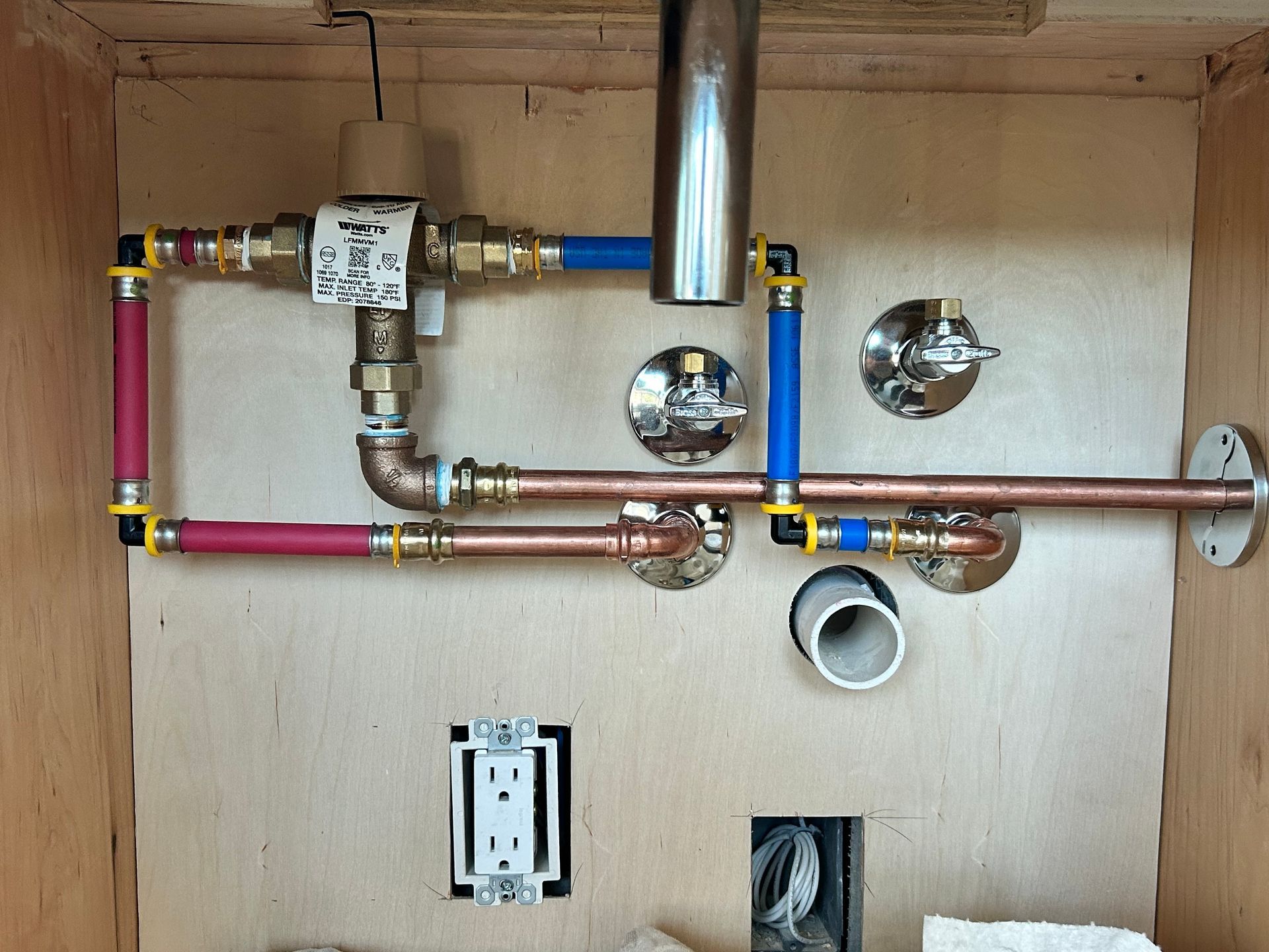 Copper and PEX plumbing pipes installed in a wooden cabinet. Red and blue PEX pipes, brass and copper fittings.