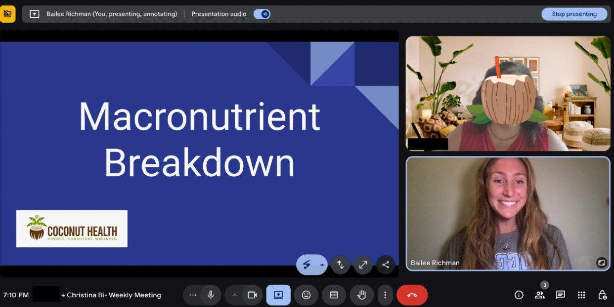 A young woman explains a diagram on a whiteboard to a seated group in a gymnasium.