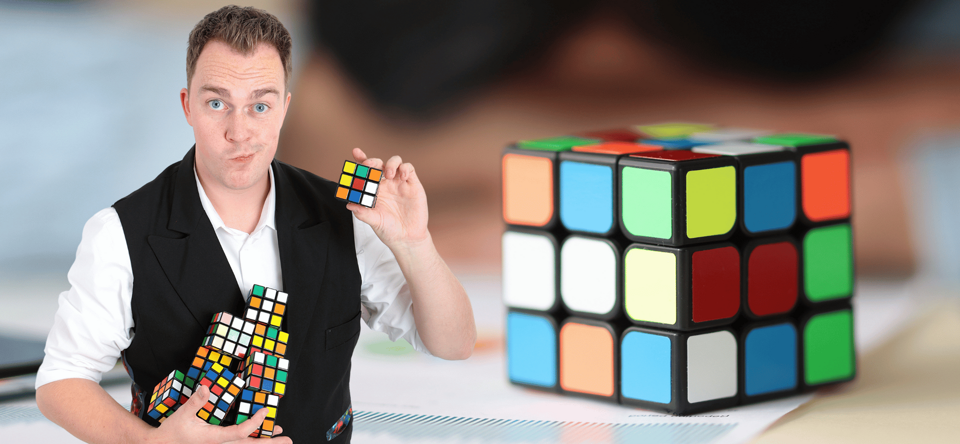 Goochelaar Marc houdt een Rubik's kubus vast voor een grote Rubik's kubus op de achtergrond.