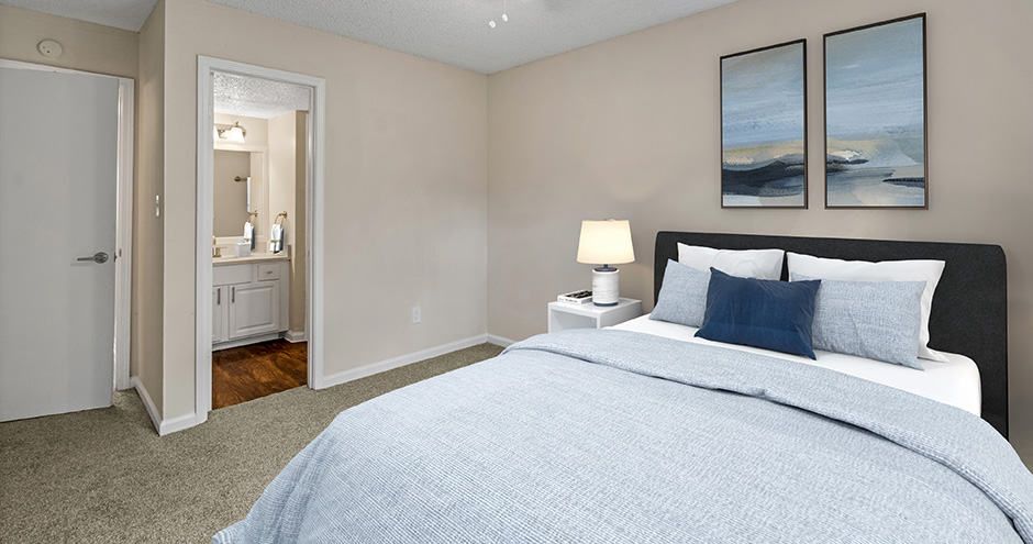 Bedroom with a bed, nightstand, and art; neutral walls, connecting to a bathroom.