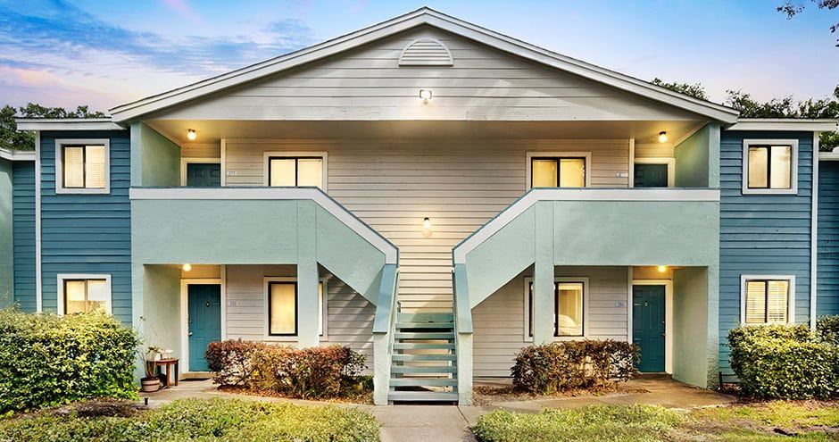 Two-story apartment building with teal and gray exterior, stairways, and windows.