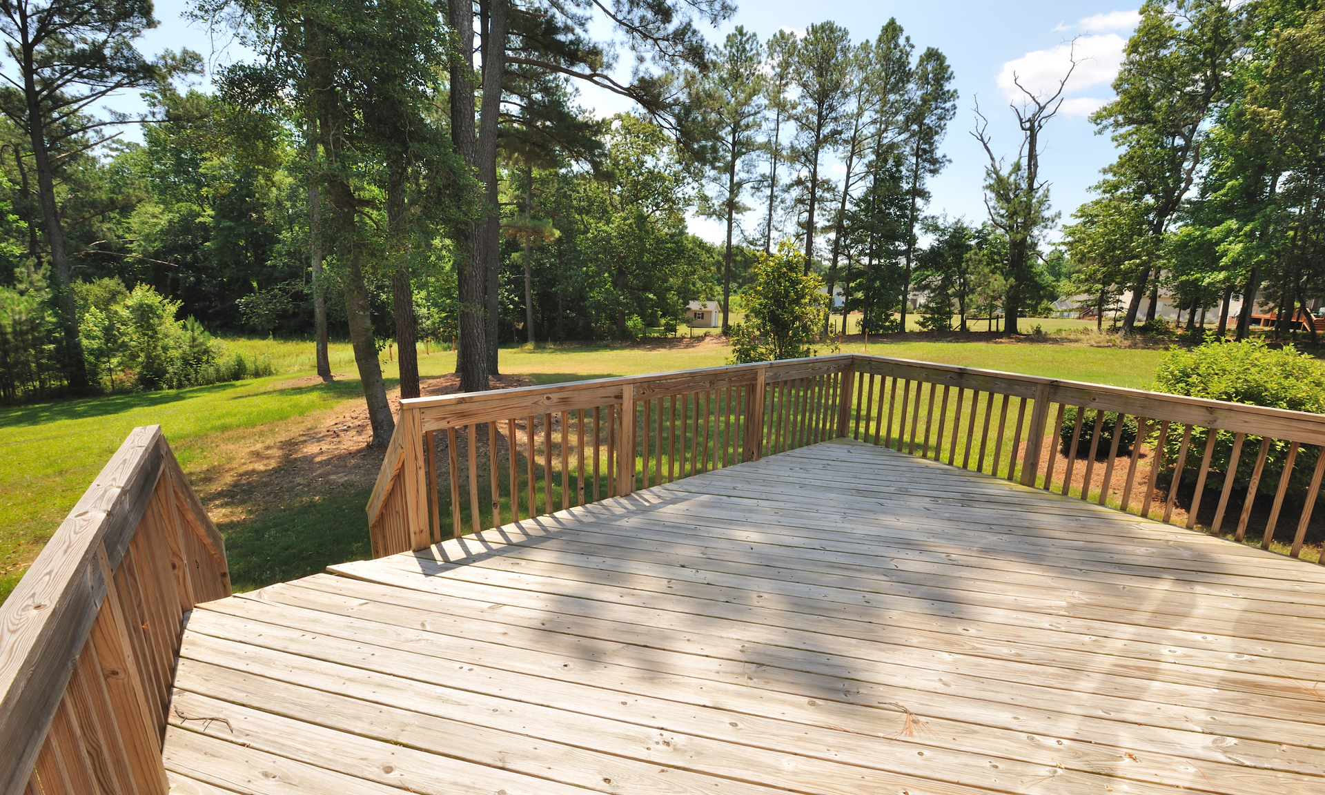 Photo of a newly built deck overlooking a beautiful green backyard with tall green trees.