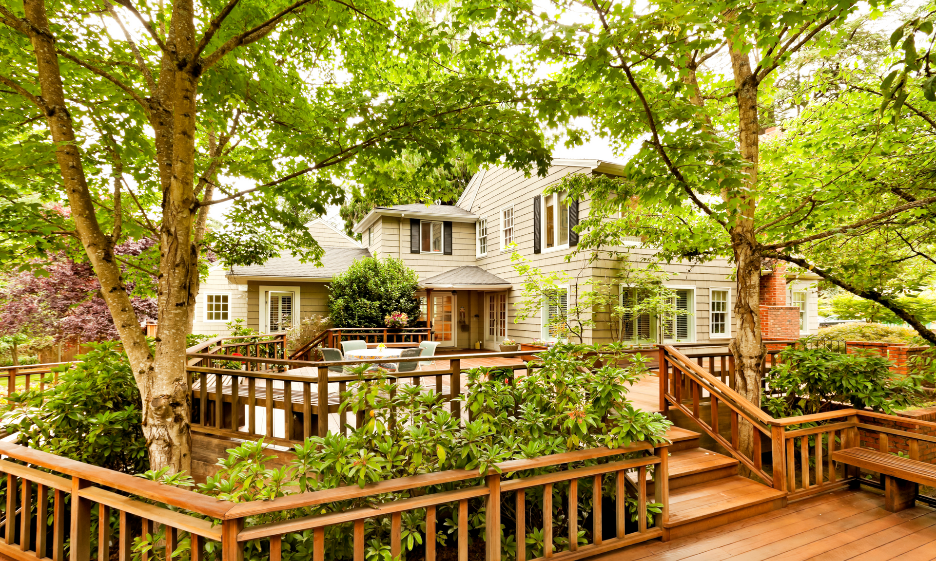 beautiful photo of a multi-level deck  with railings that has a bunch of trees and greenery surrounding the deck.