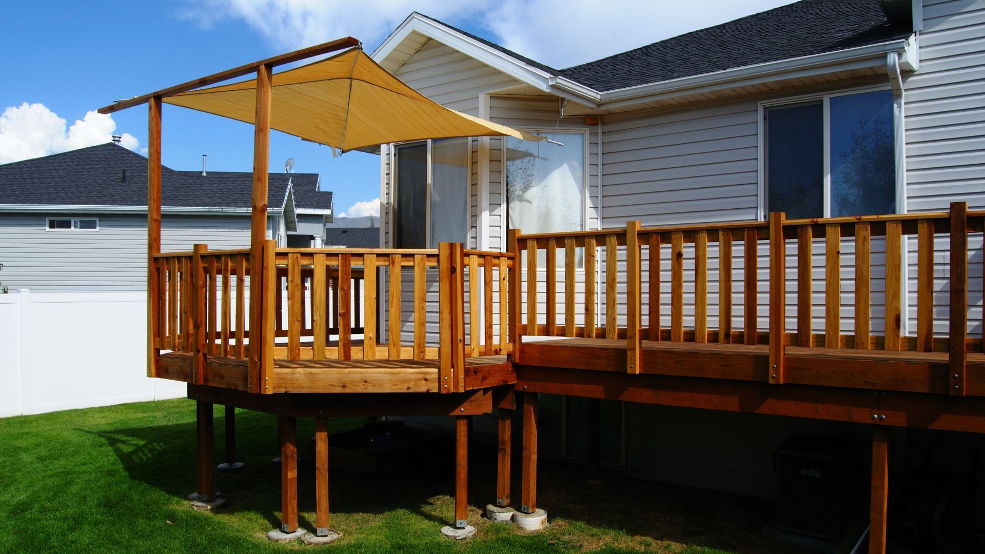 A new wooden deck with railings and sunshade is in a suburban Athens, GA, backyard.