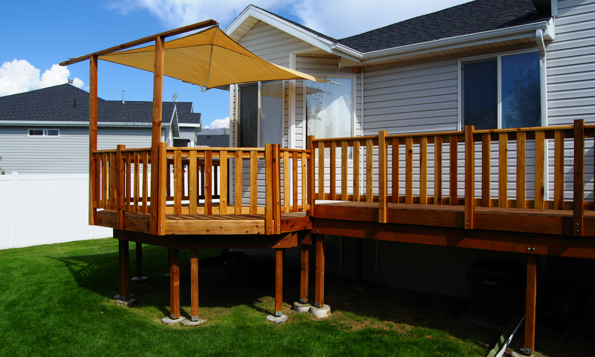 photo of an elevated deck on the back of a house with a deck roof on a small portion of the deck. It is a beautiful day out in the photo with a clear blue sky and bright green grass.