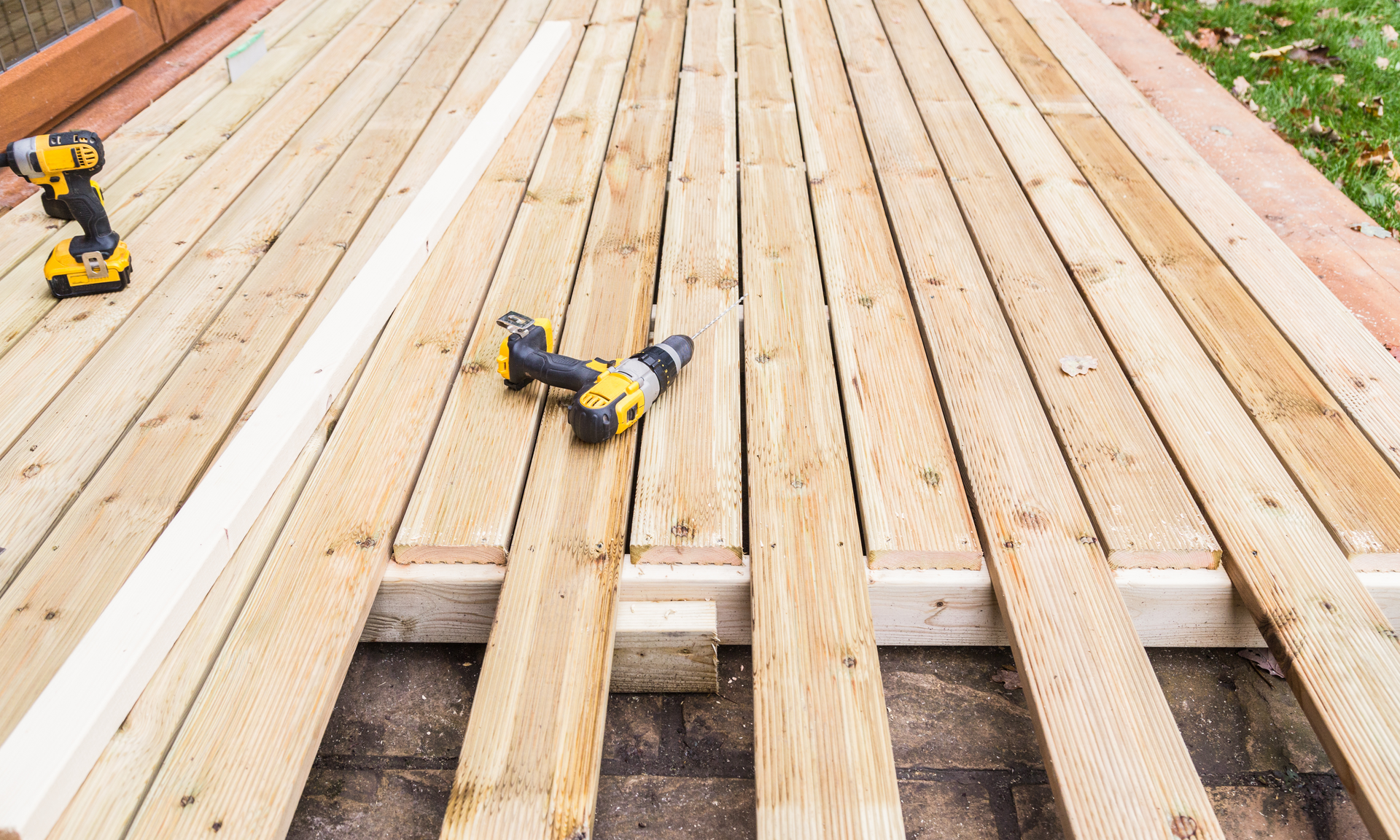 A photo of a deck in the process of being built. The boards are laid down on the frame and they are being screwed into down with a drill.