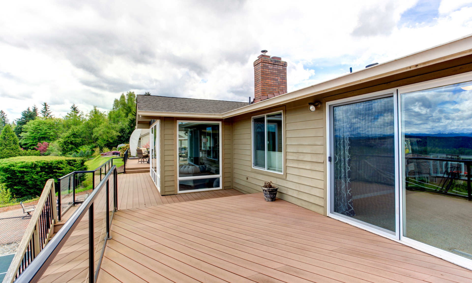 photo of a large multi-level deck connected to a house with a sliding back door. The deck is made out of composite materials and has a glass railing.