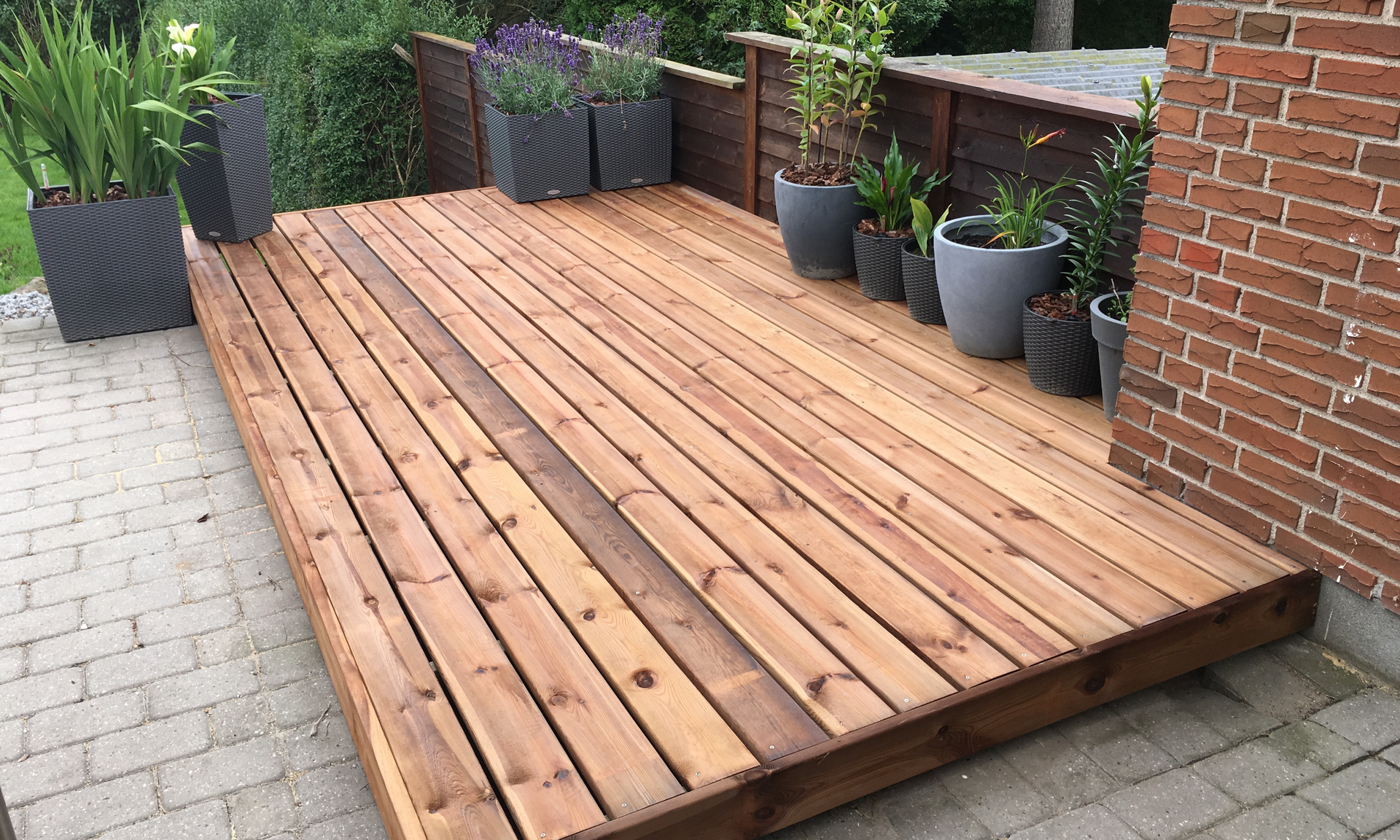 photo of a small deck built on top of a paver patio. The deck is used for showcasing plants and flowers.