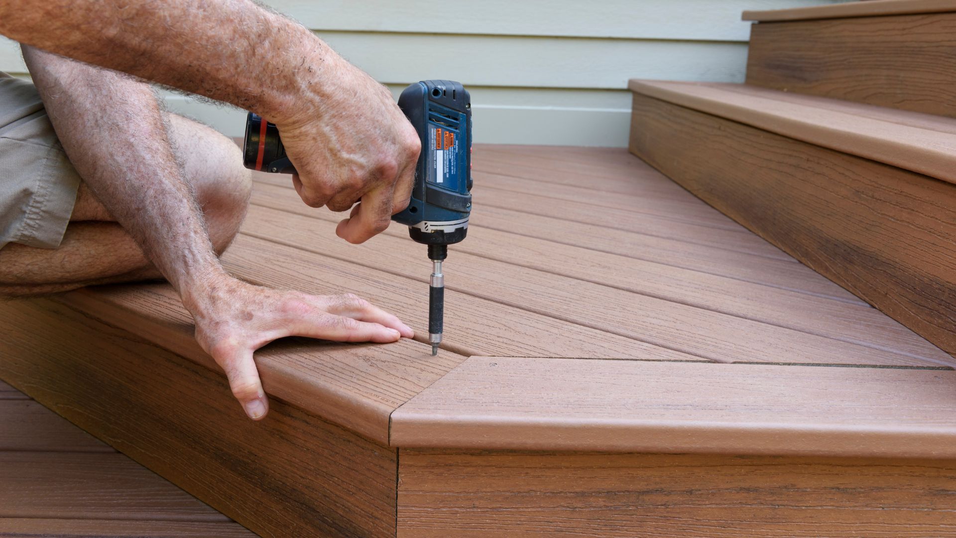 A person using an electric drill to install deck boards on stairs in Athens, GA.