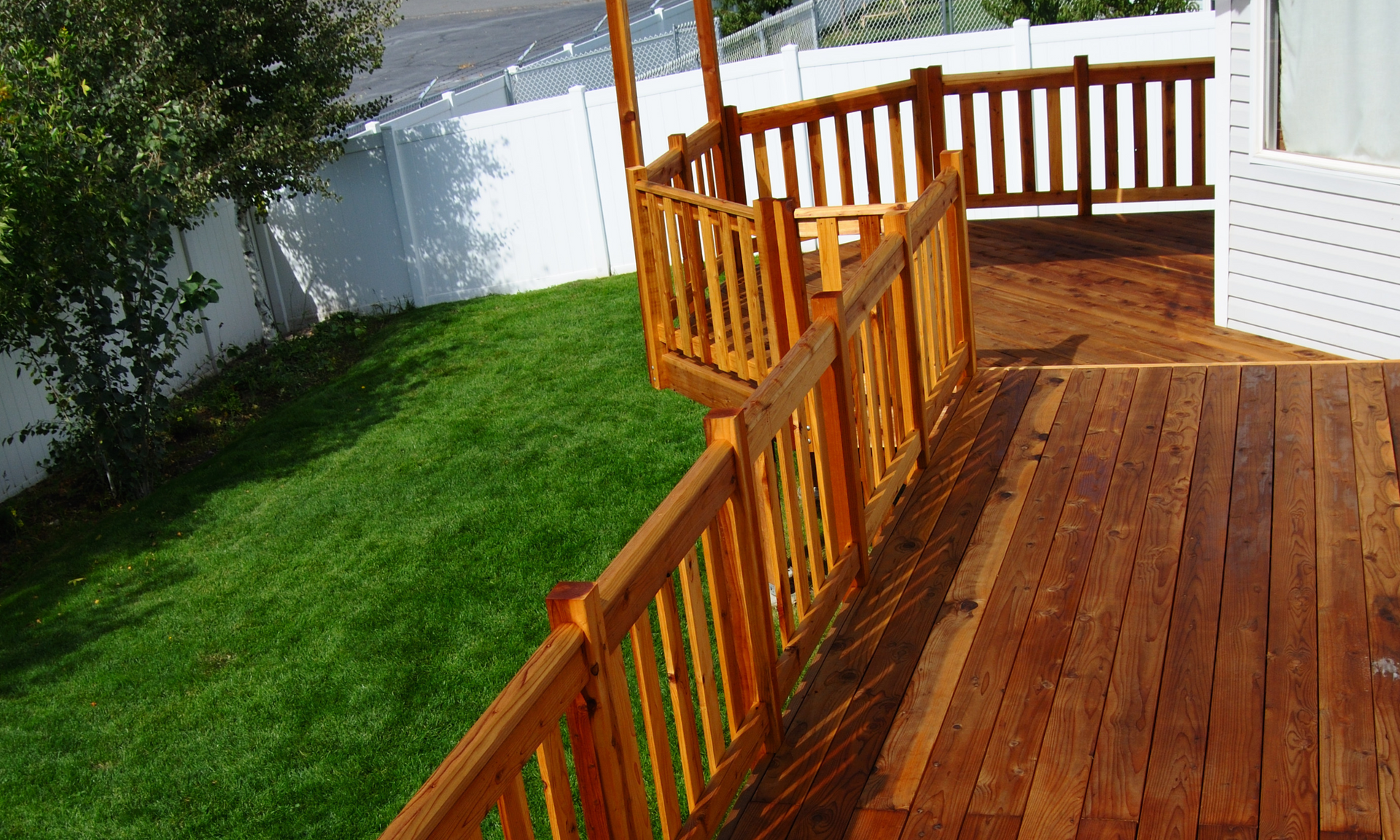 photo of a second-level deck with a railing and a covered gazebo portion next to luscious green grass and a white PVC hence in the background.