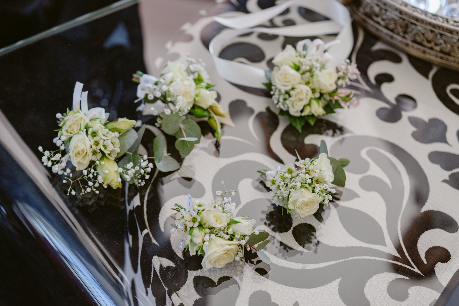 Five small white rose bouquets with greenery and white ribbons on a patterned surface.