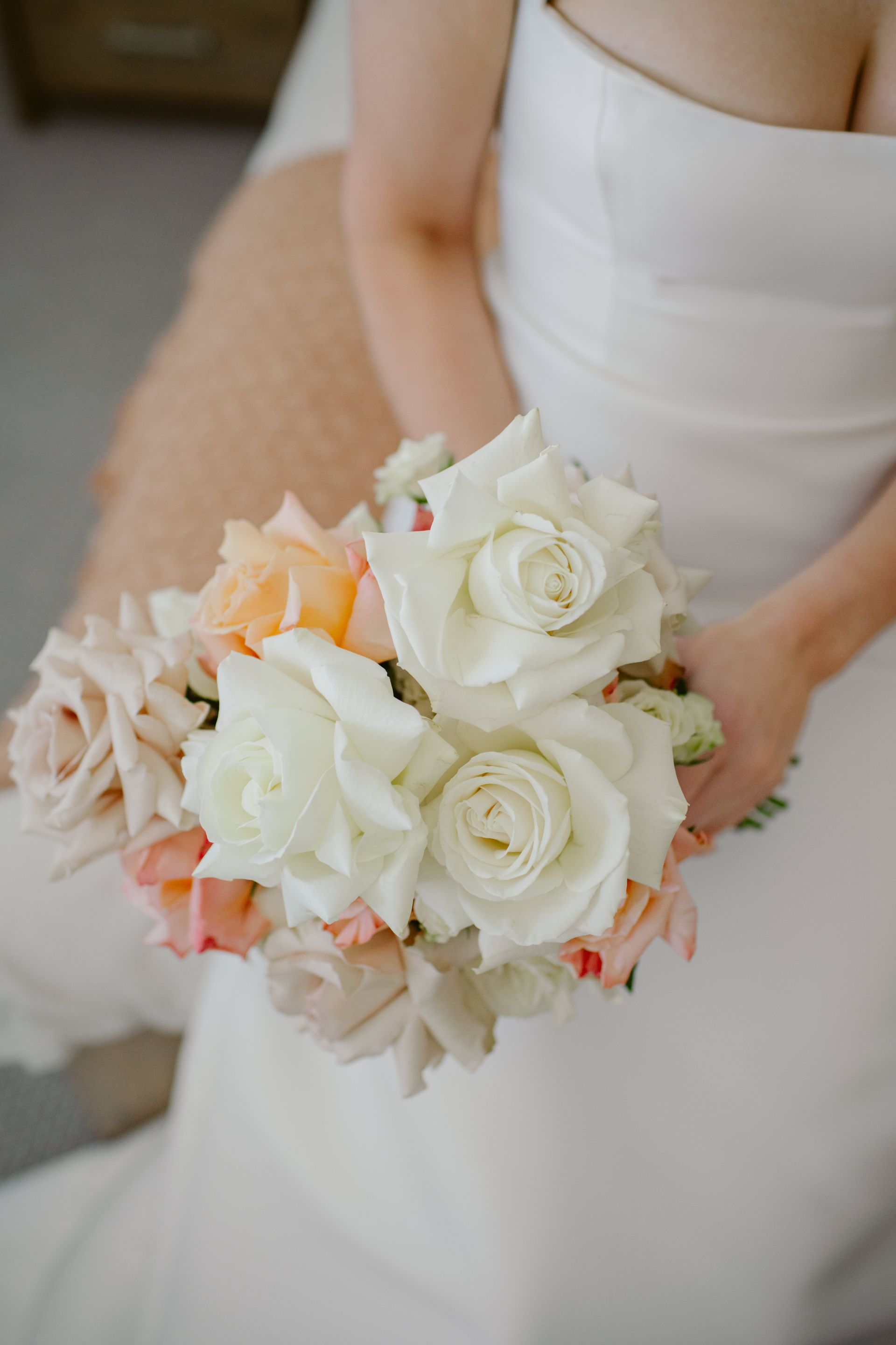 Bride in white dress holding a bouquet of white and peach roses.