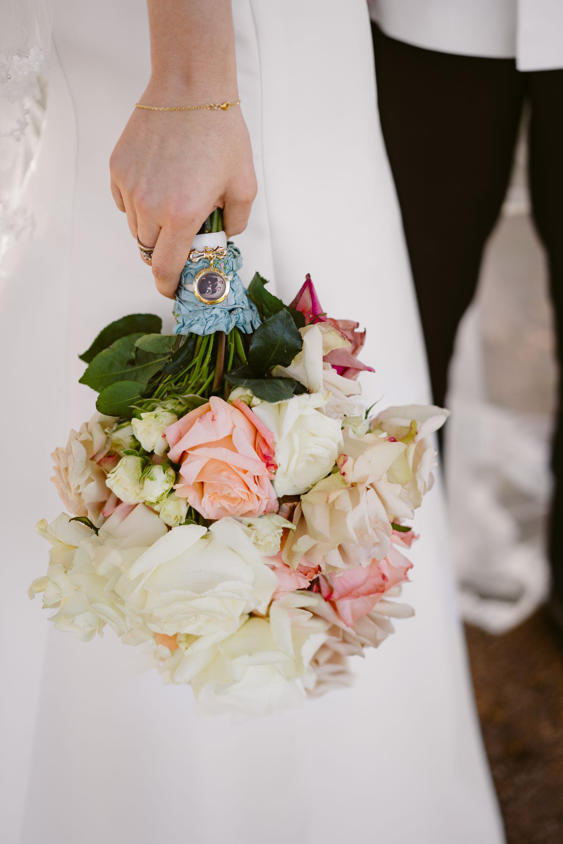 Bride holding a bouquet of white and peach roses, with a small framed photo on the handle.