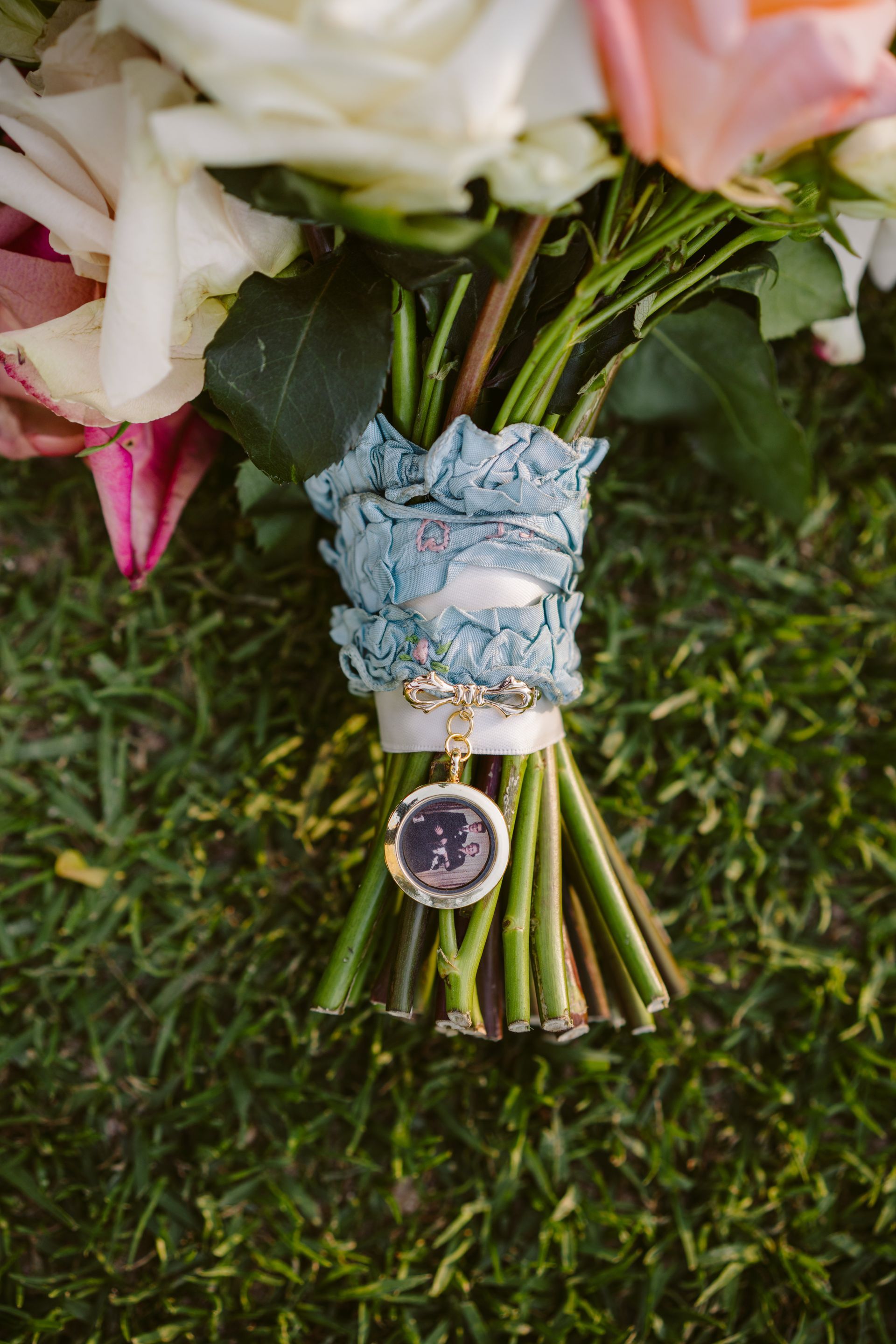 Wedding bouquet tied with blue lace and a pendant, resting on grass.