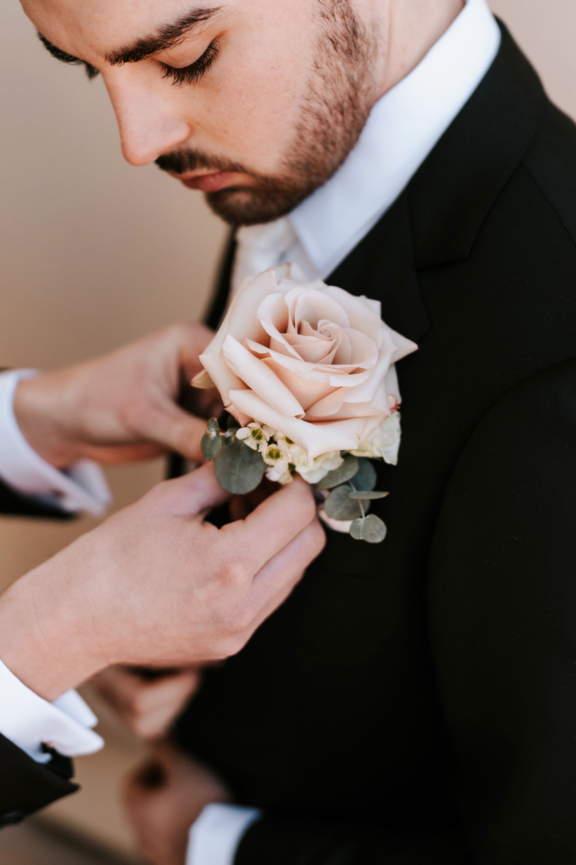 Person in black suit having a blush rose boutonniere pinned on his lapel.