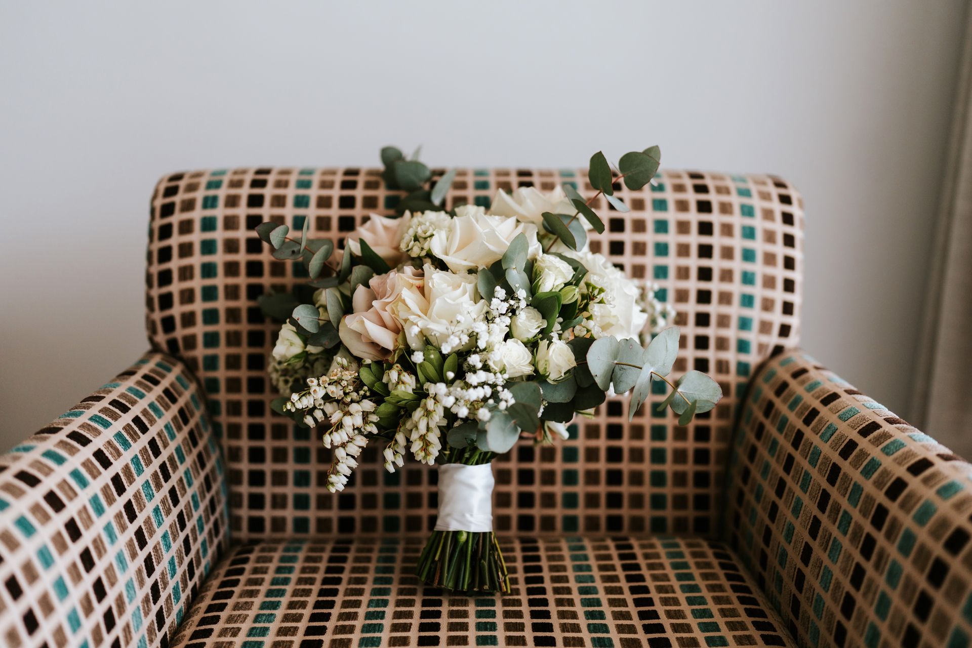 Wedding bouquet on patterned armchair. White and cream flowers with greenery, tied with ribbon.