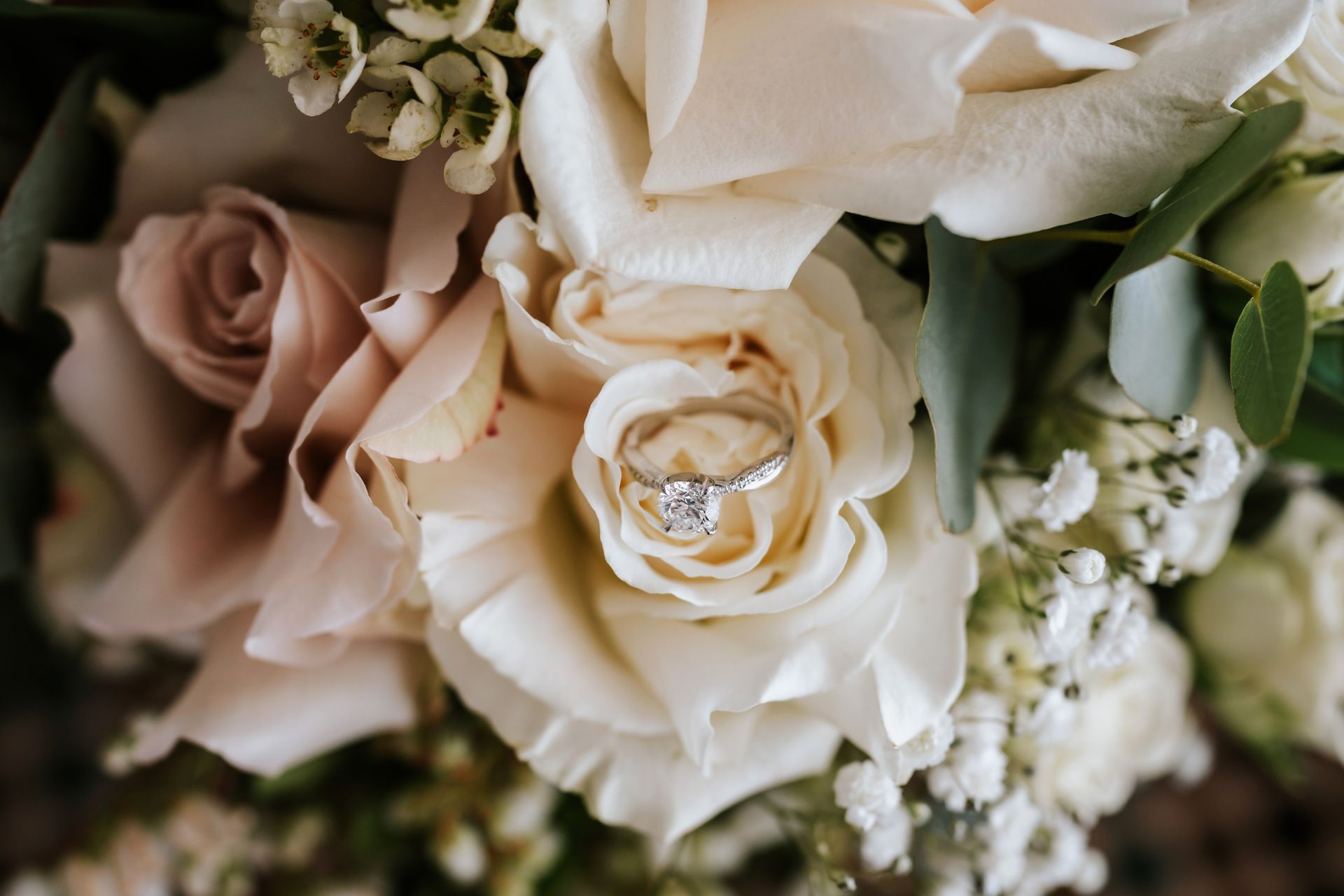 Engagement ring on a cream rose in a bouquet of flowers.