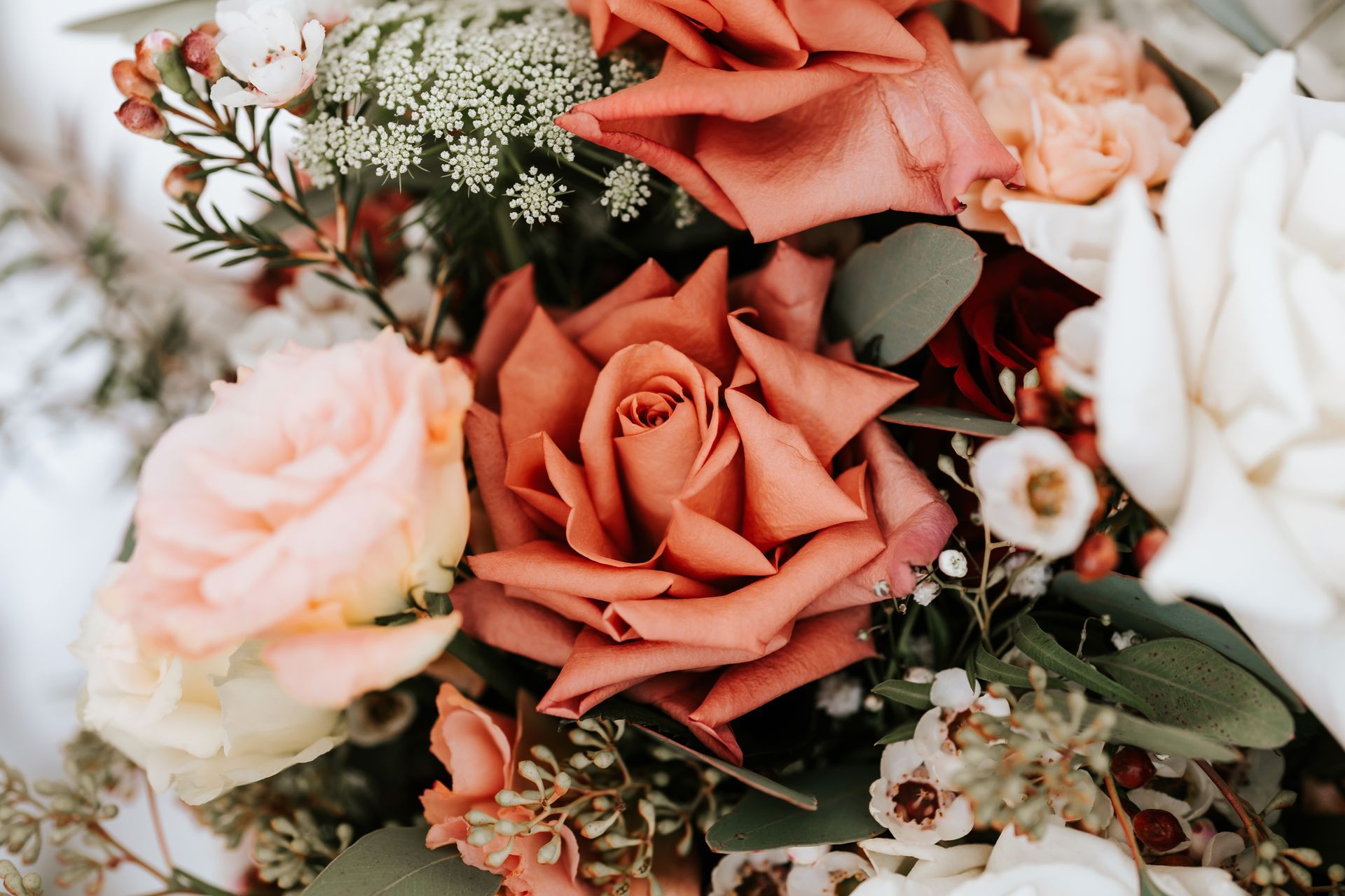 Close-up of a bouquet with rust, blush, and white roses, green foliage, and tiny white flowers.