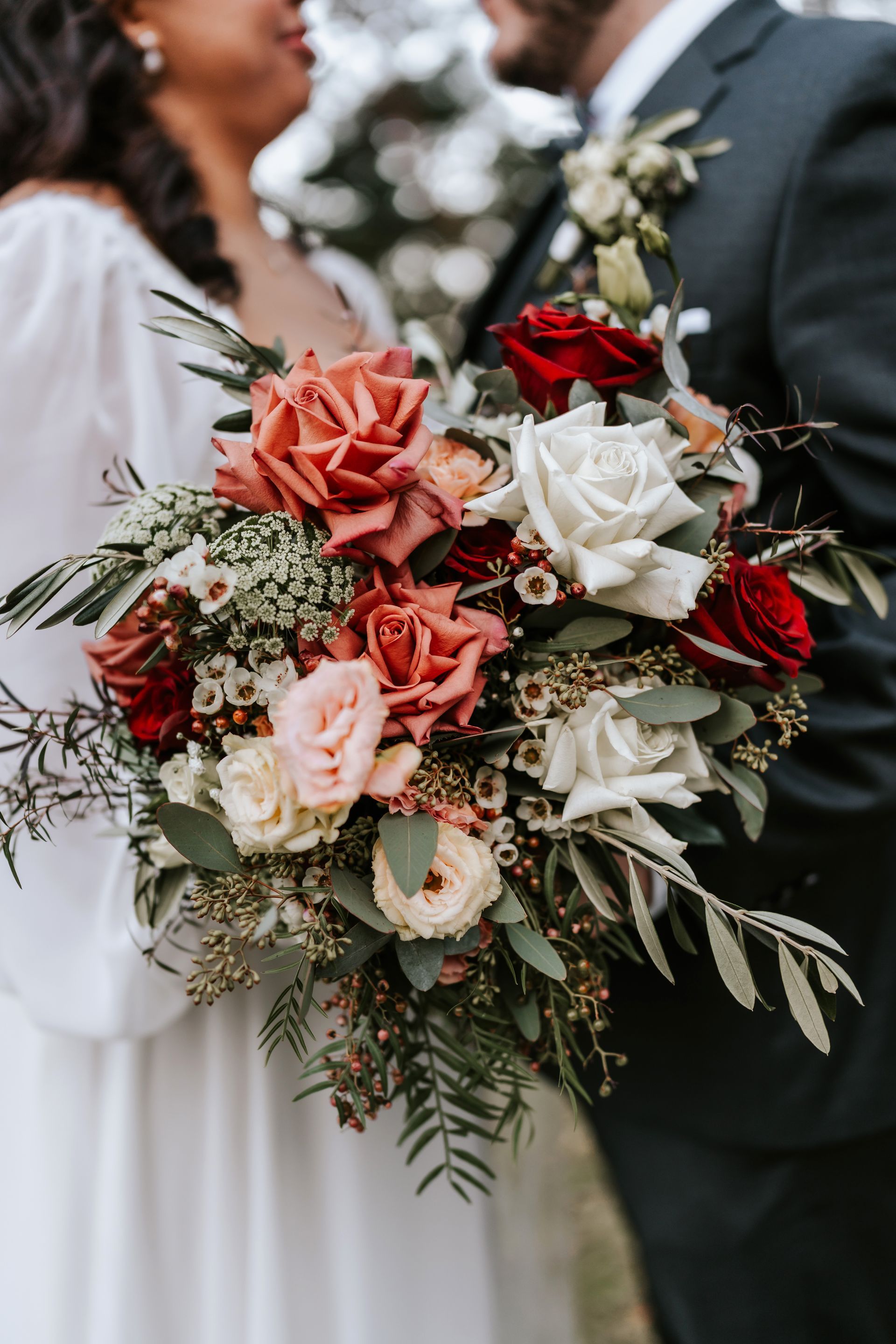 Bride and groom holding a bouquet of red, peach, and white roses; wedding.