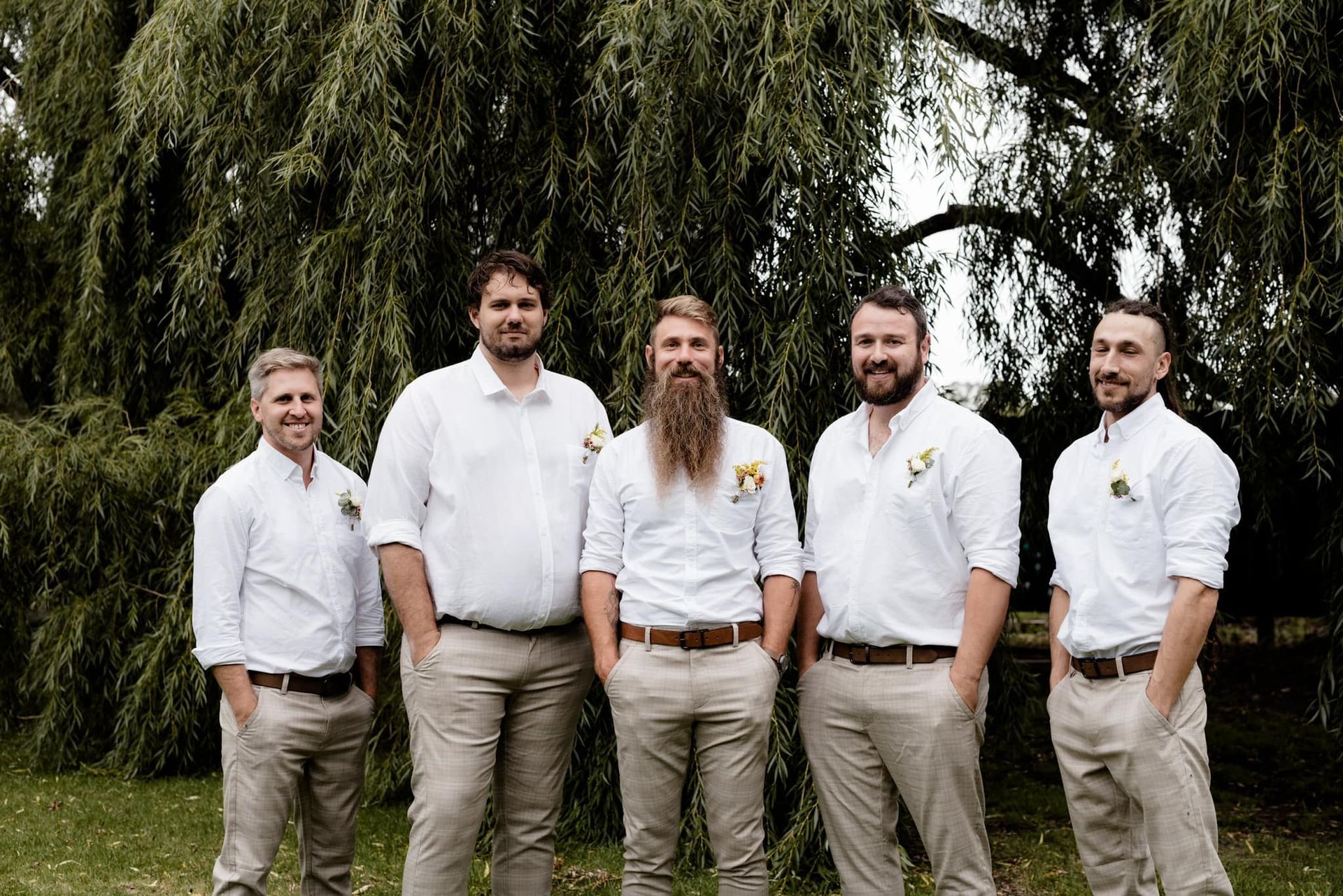 Five men in white shirts and tan pants pose outdoors, with a large tree in the background.
