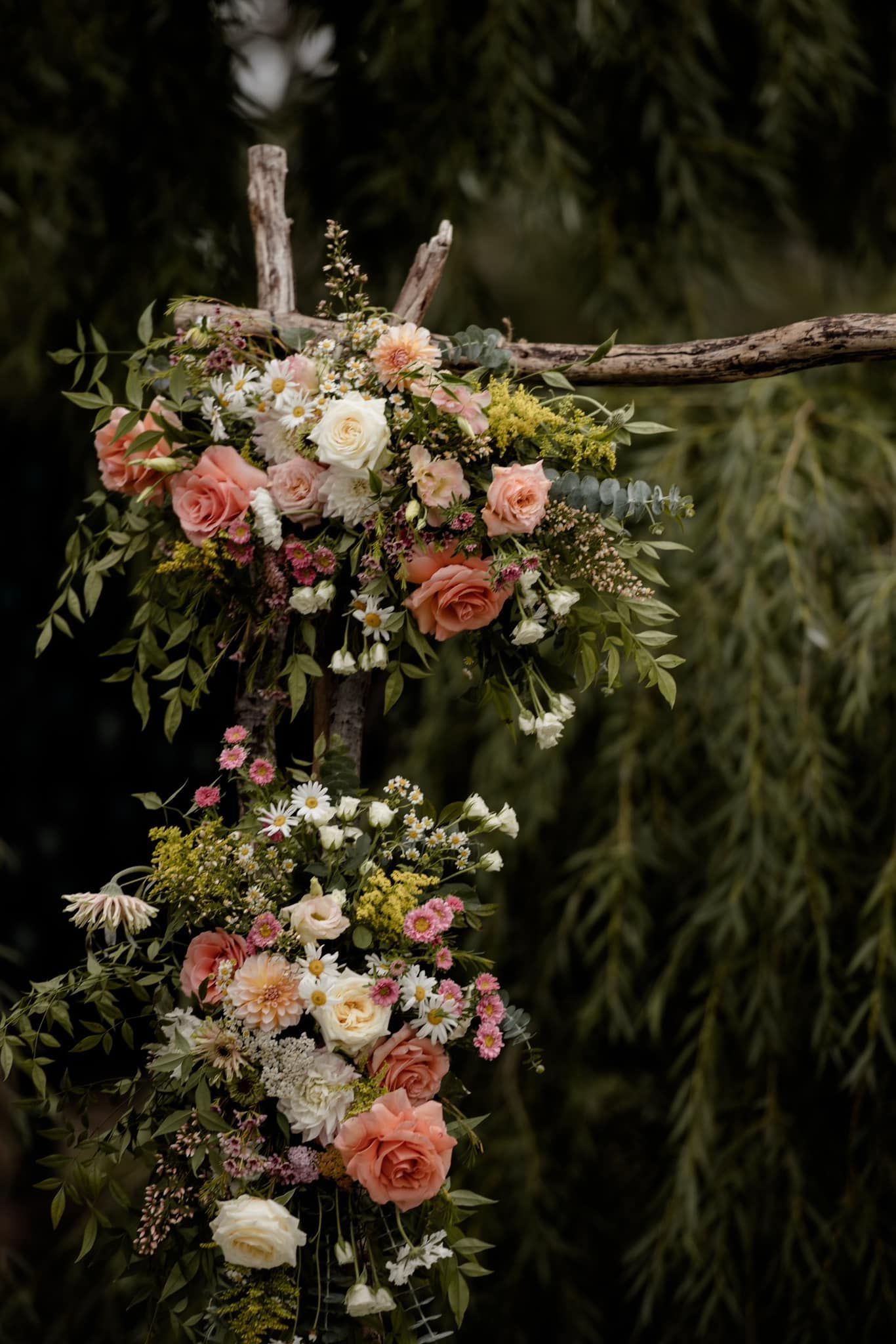 Floral arch with peach and white roses, green foliage, outdoor setting.