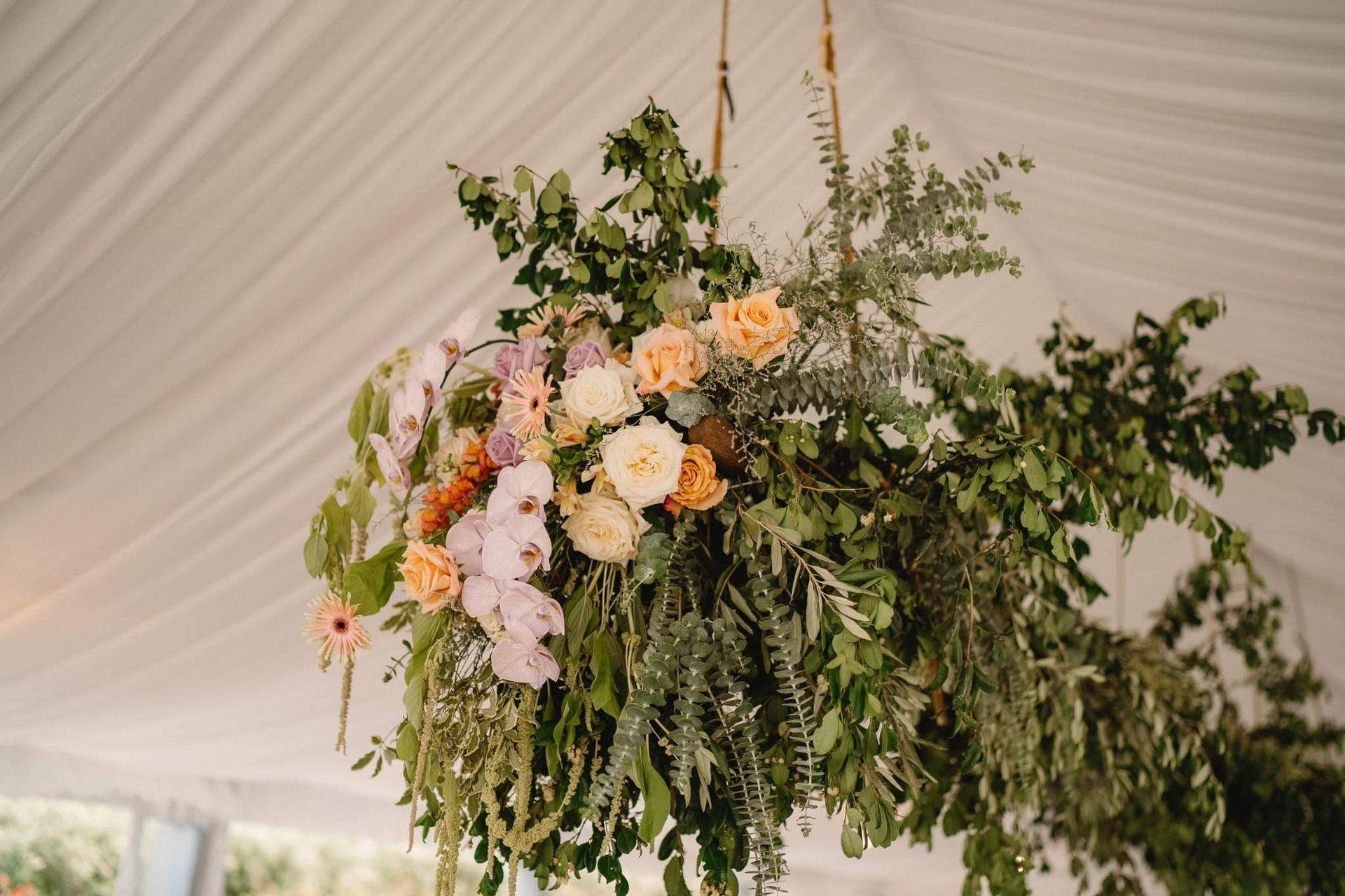 Hanging floral arrangement with various flowers, greenery, and a white tent background.