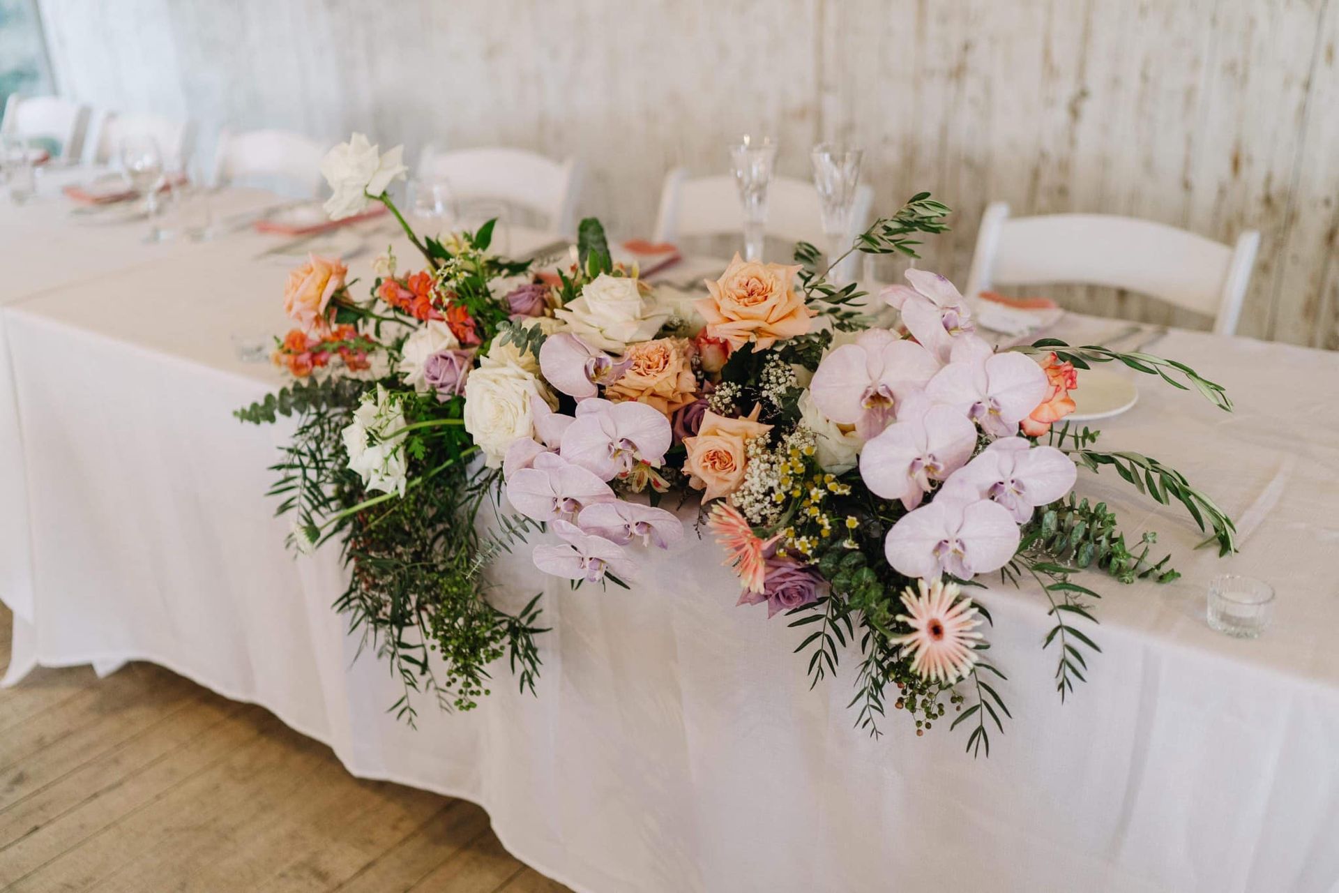 Wedding table with colorful floral centerpiece: peach, orange, and lavender blooms with greenery.