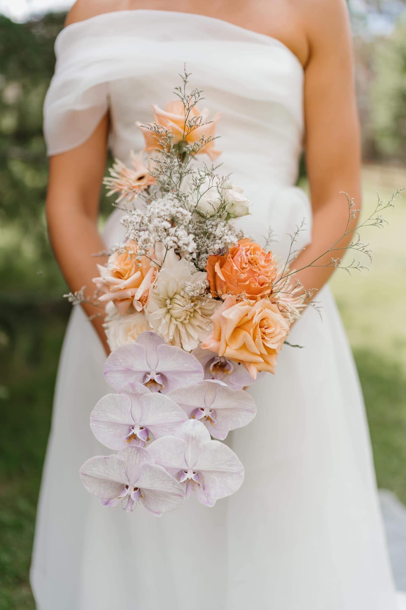 Bride holding a cascading bouquet of peach and white flowers. Outdoors.