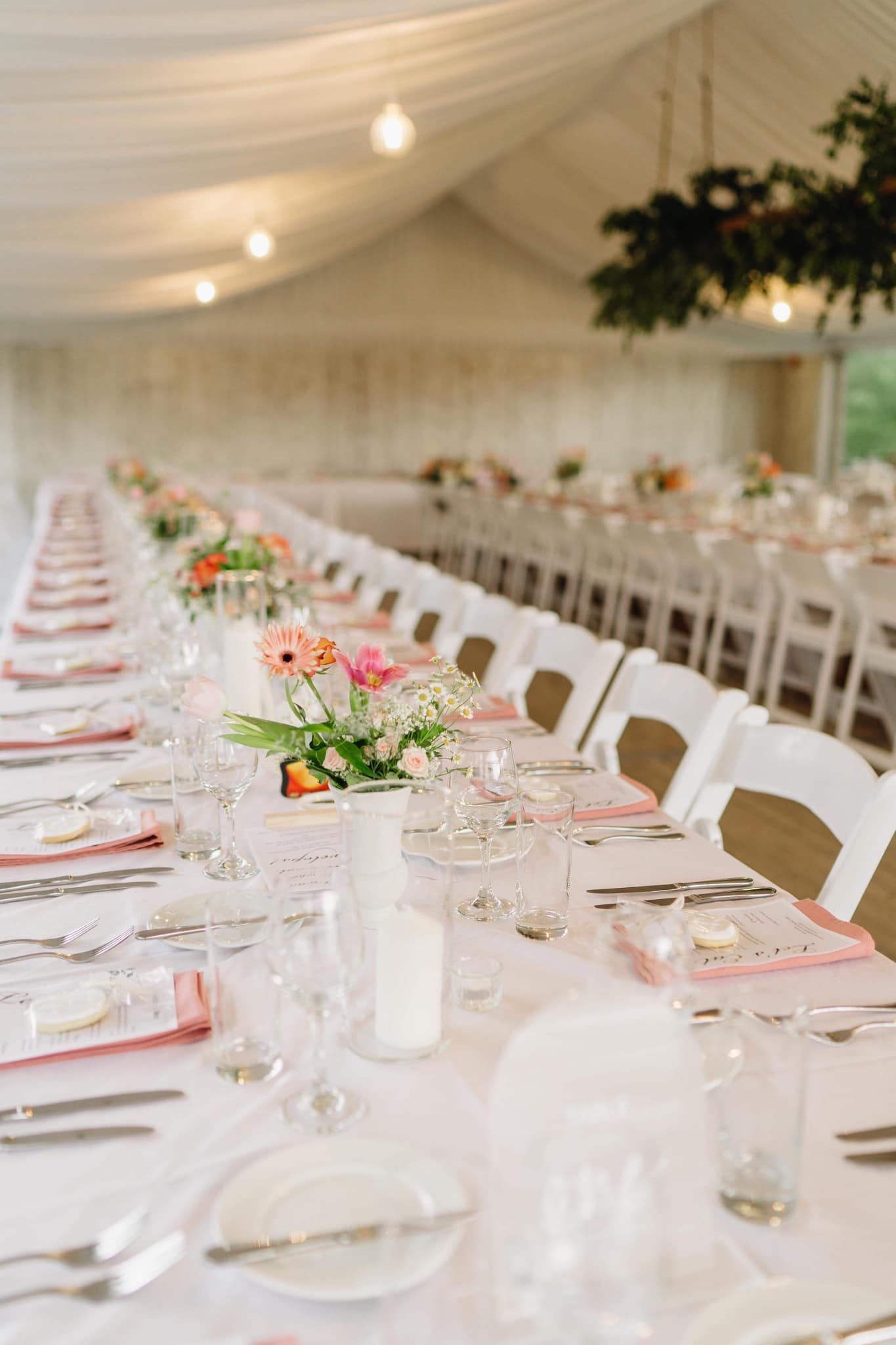 Long table set for a wedding reception with white chairs, linens, and floral centerpieces.
