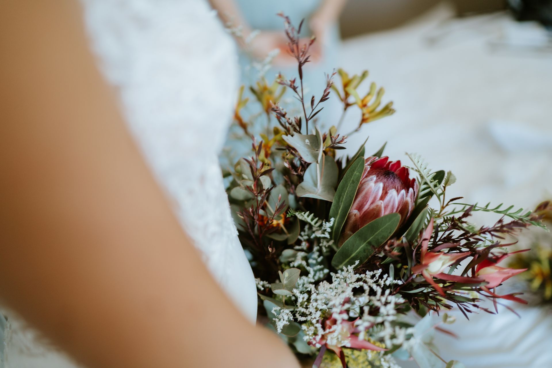 Bride in white dress holds a bouquet with a protea flower.