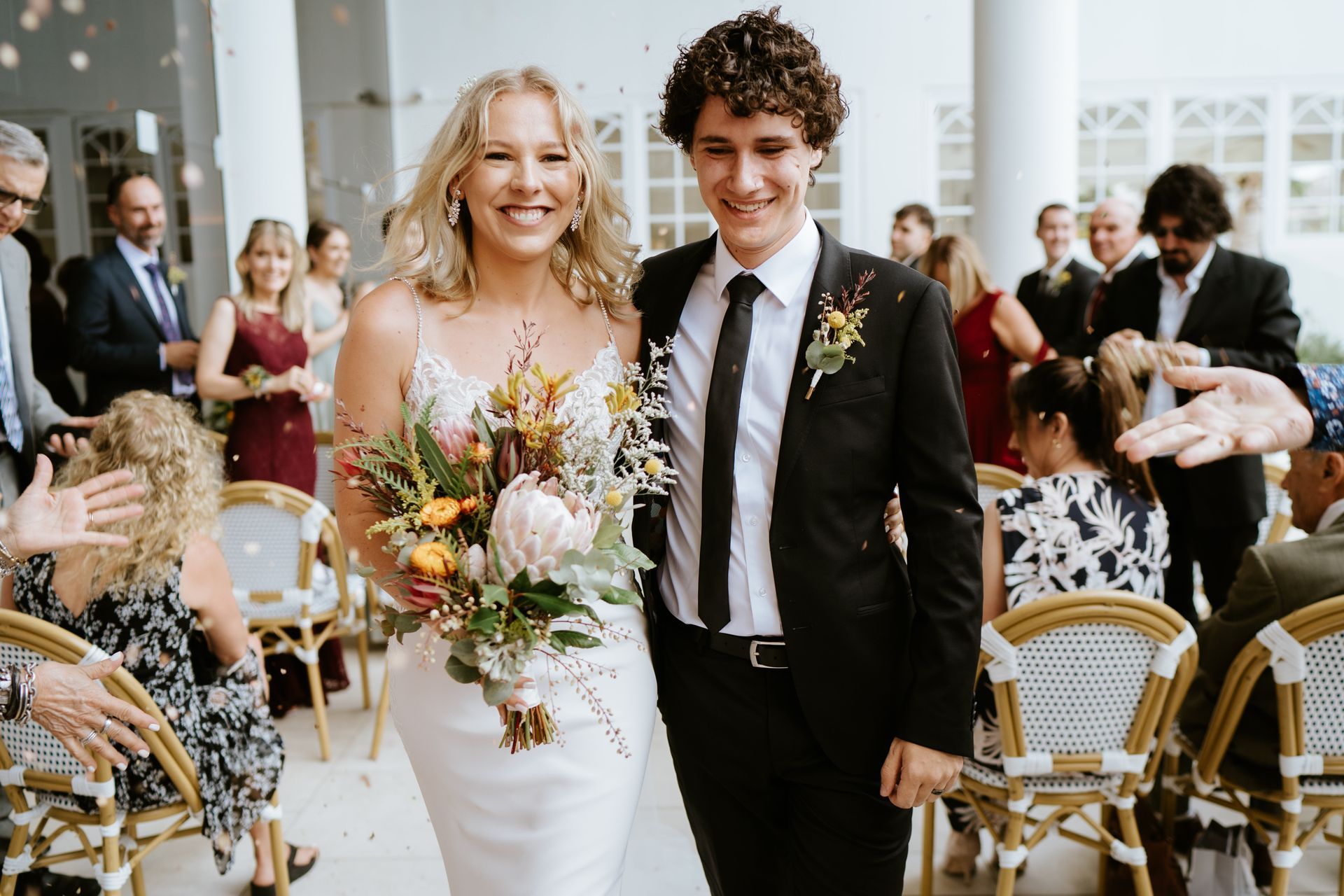Newlyweds smile while walking down the aisle, showered with confetti.