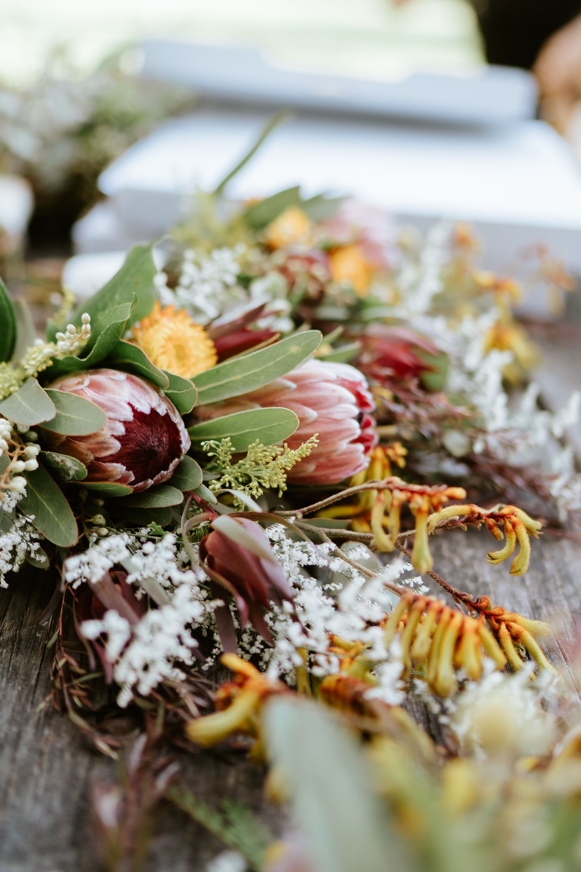 Close-up of a floral arrangement with protea and other colorful wildflowers on a rustic wooden surface.