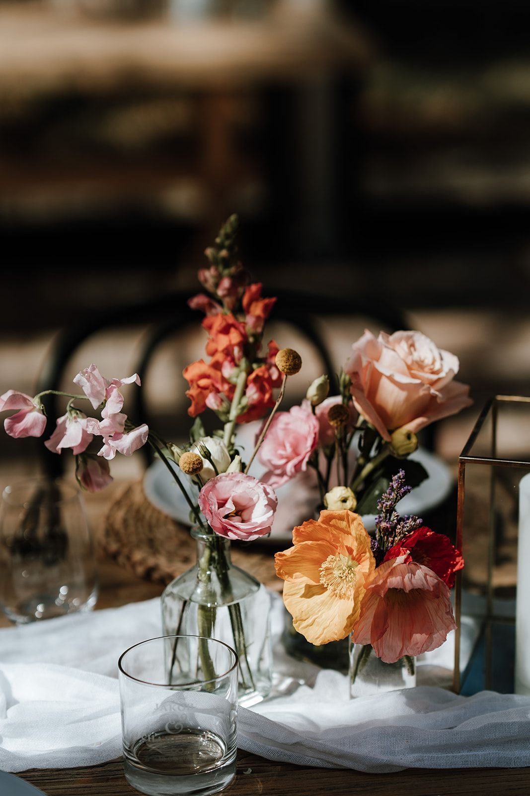 Floral centerpiece with pink, orange, and red flowers in glass vases on a table.