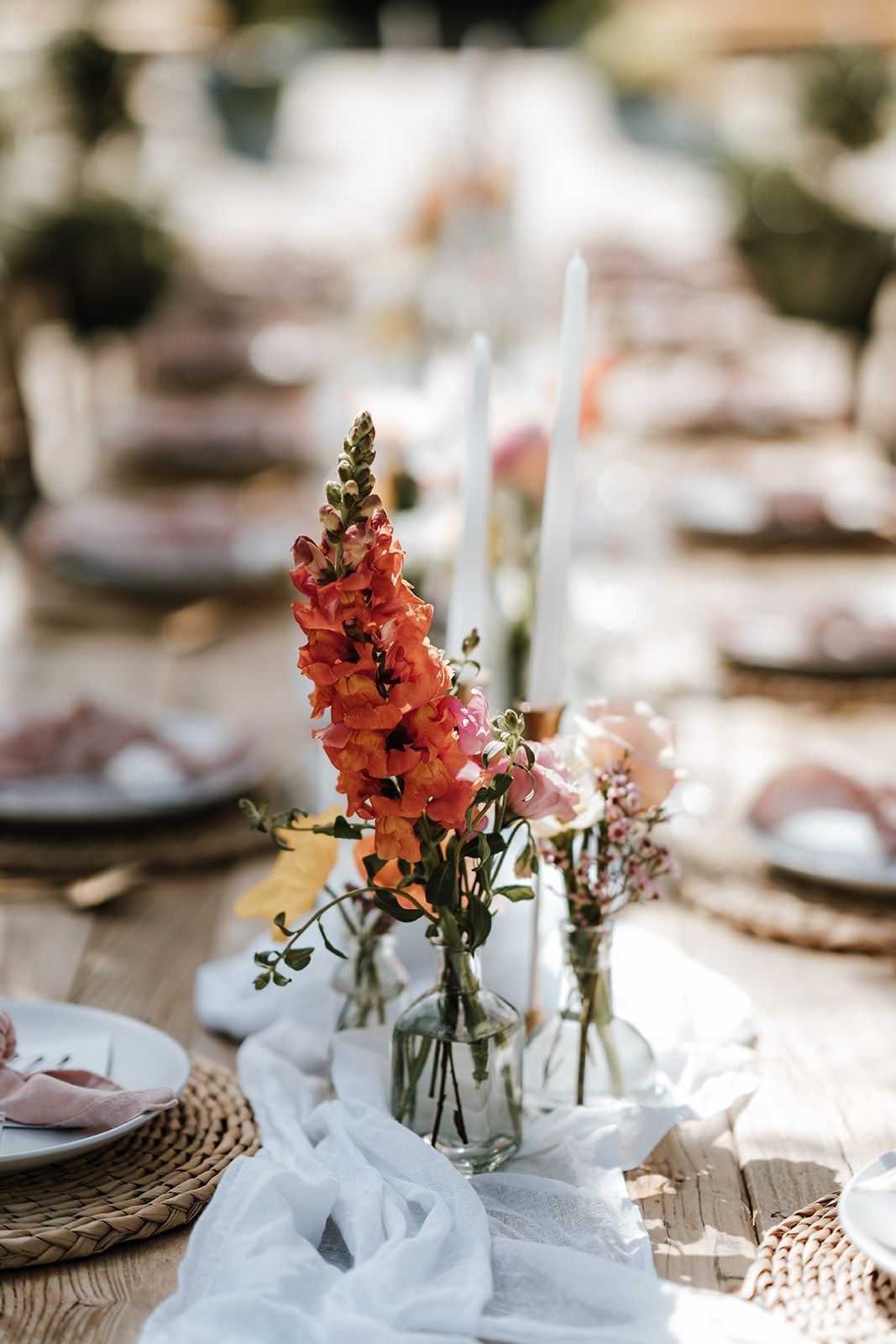 Table setting with orange and pink flowers in glass vases, outdoor dining.
