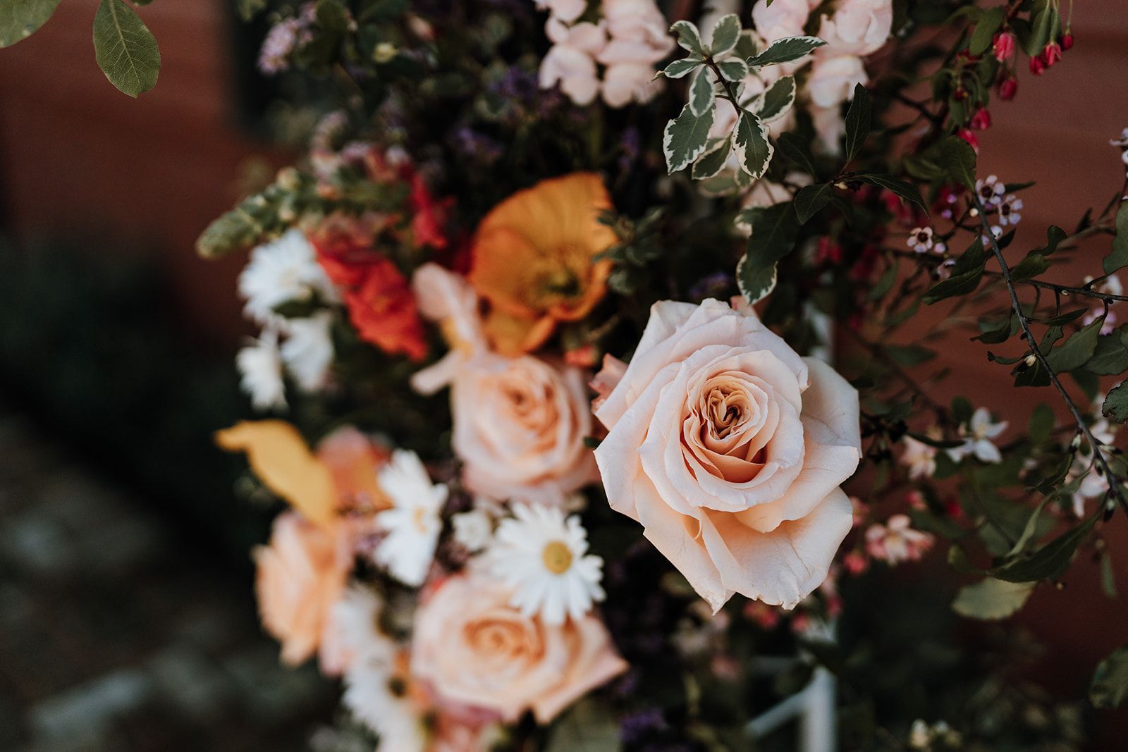 Close-up of a floral arrangement featuring peach roses, daisies, and other colorful blooms.