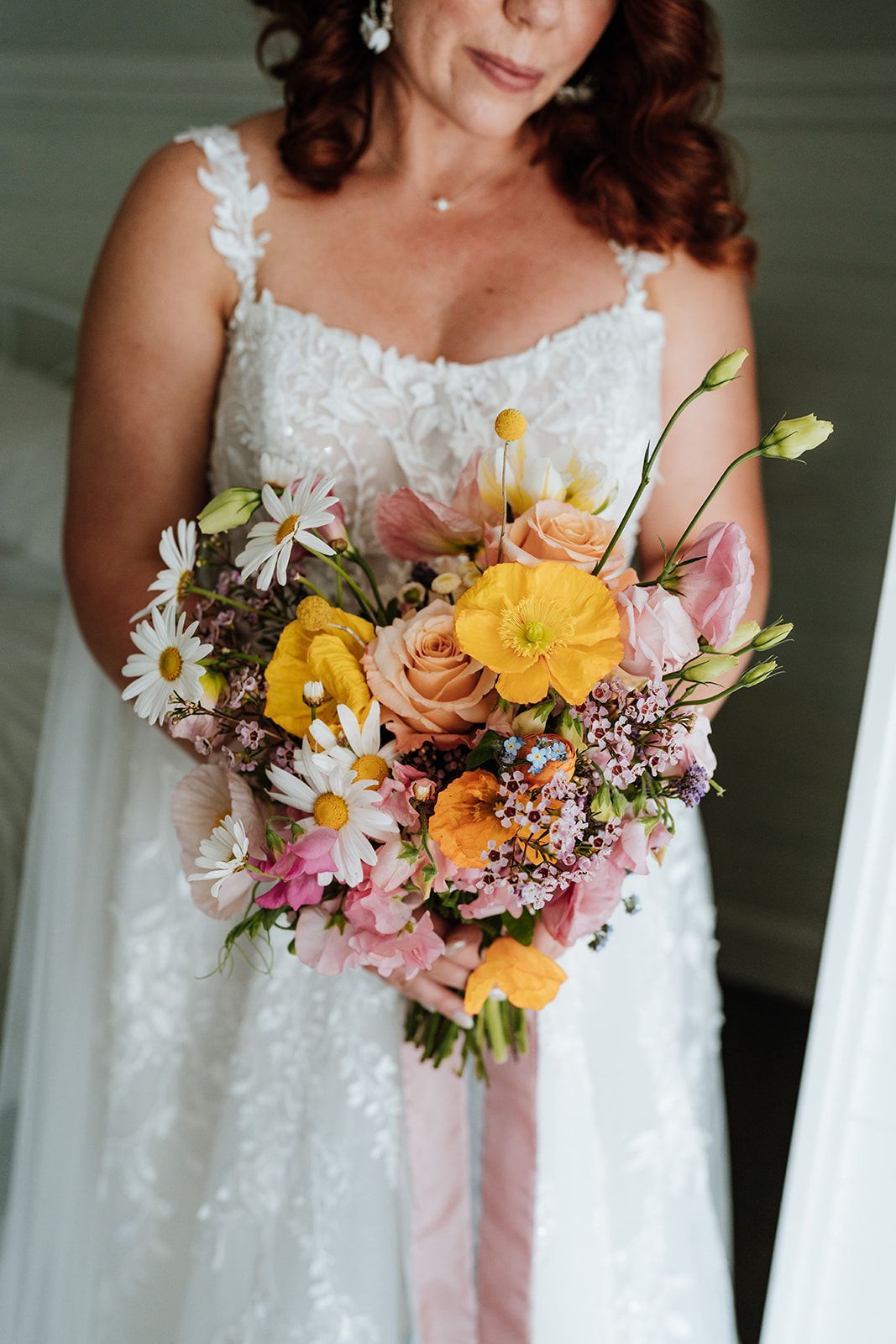 Bride holding colorful bouquet, wearing a white gown, and looking down.