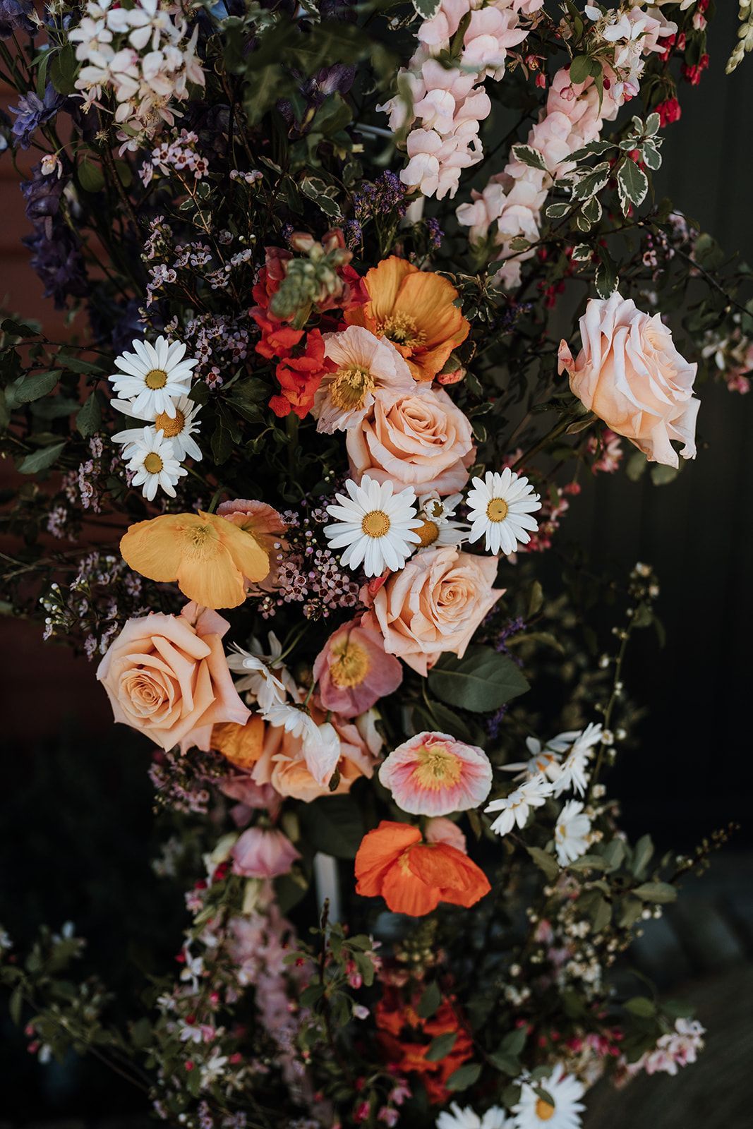 Assorted flowers in peach, orange, red, and white, arranged on a dark background.