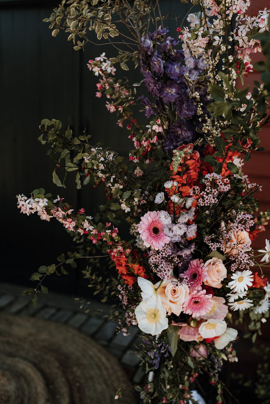 Floral arch with pink, red, purple, and white flowers, set against a dark green backdrop.