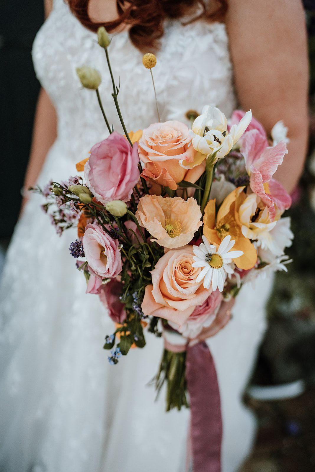 Bride holding a colorful bouquet of flowers: roses, daisies, and orchids.